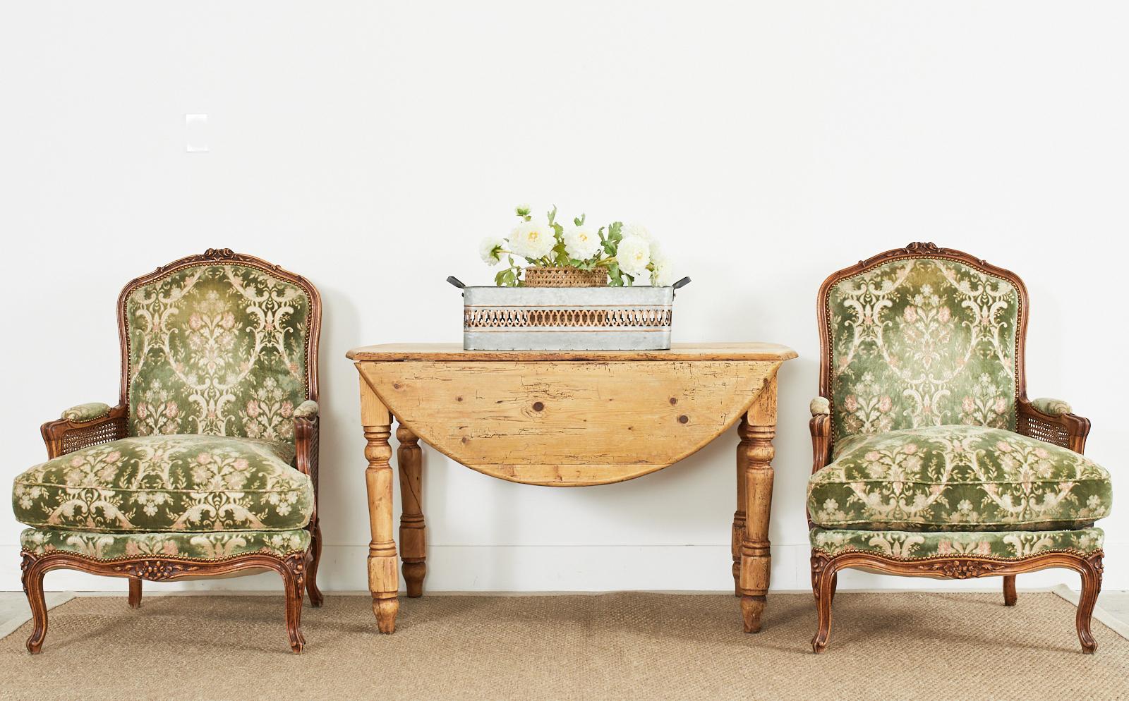 Gorgeous pair of country French provincial bergere armchairs or lounge chairs crafted from walnut. The chairs feature a beautifully carved frame with molded arms and classic flat backrest. The arms have double caned sides and a generous seat with a