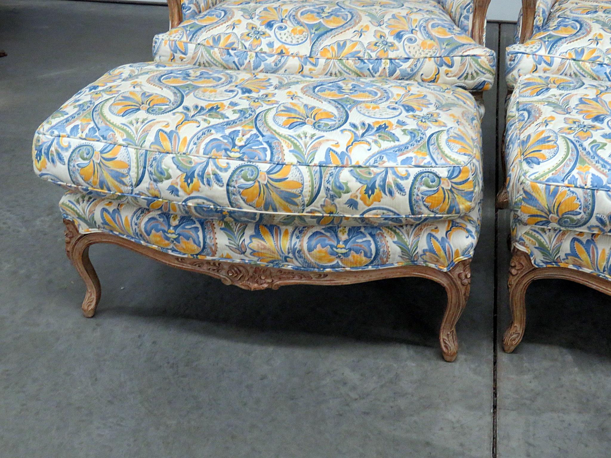 Pair of Country French style distressed finish wingback chairs and ottomans with textured upholstery. The chairs each measure 42