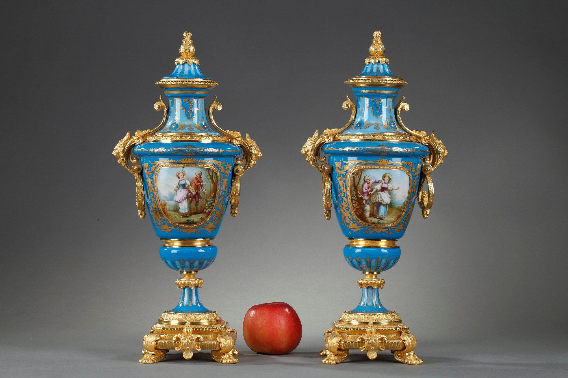 Paire de vases couverts en porcelaine polychrome de style Sèvres avec montures en bronze doré. 

La base repose sur quatre pieds griffes et des cartouches en forme de cuir découpé ornés de coquillages. Les poignées en bronze doré sont décorées