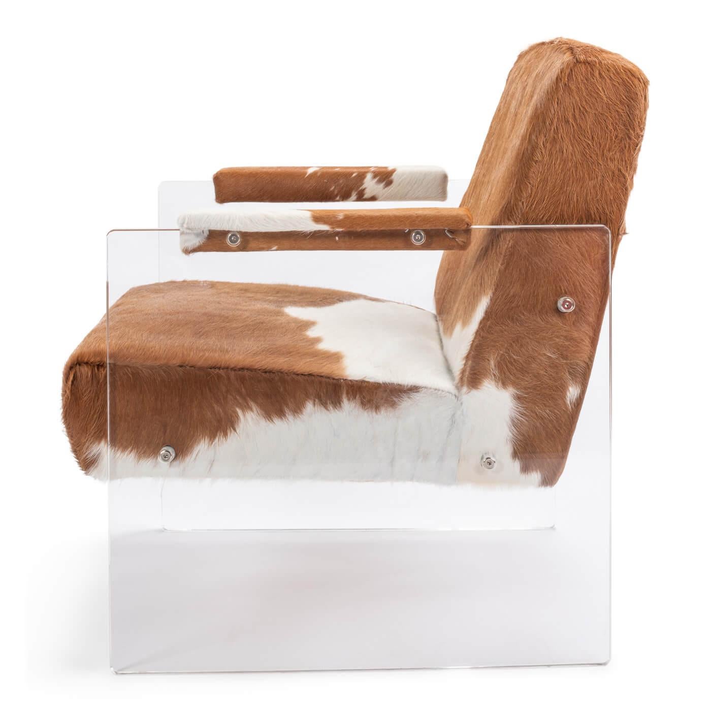 A cowhide and lucite armchair with a modern vintage-western feel, featuring luxe lucite acrylic sides and a brown with white cowhide seat and back. A unique combination of materials makes this piece a true statement piece in any room. Cowhide padded