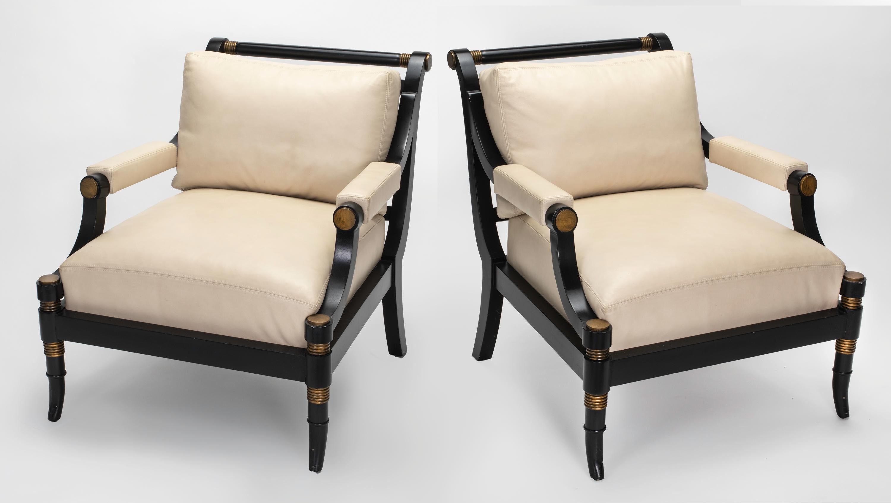 Pair of Klismos style ebonized wood frame arm chairs with bronzey gilt accent trims. Newly covered in soft cream color leather seat and back cushions. Back cushions are down feather filled. Back of the chair is cut design fret work. Arm caps also in