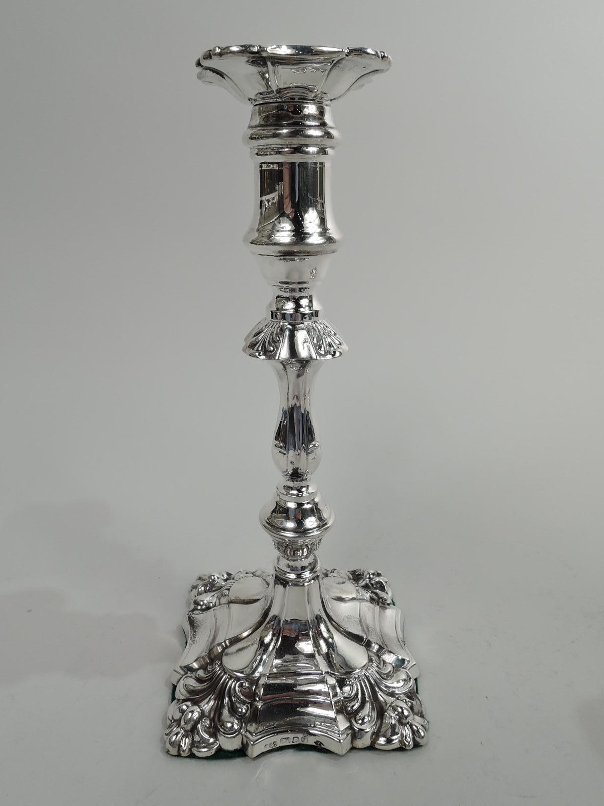 Pair of English Georgian Rococo sterling silver candlesticks, 1961. Each: Spool socket with detachable bobeche on knopped and baluster shaft with alternating lobes and flutes on stepped square foot with same. Corner leaf ornament. Fully marked