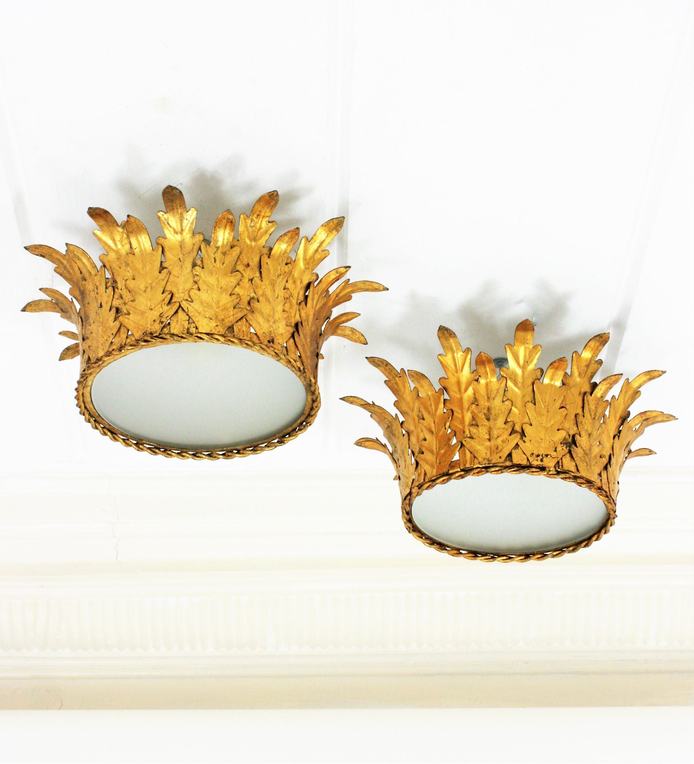 Two Neoclassical style hand-hammered gold leaf gilt iron crown shaped flush mounts or pendants, France, 1940s.
These flush mounts feature gilt iron structures adorned by foliage details. They have frosted glass diffusers that allow to disperse a