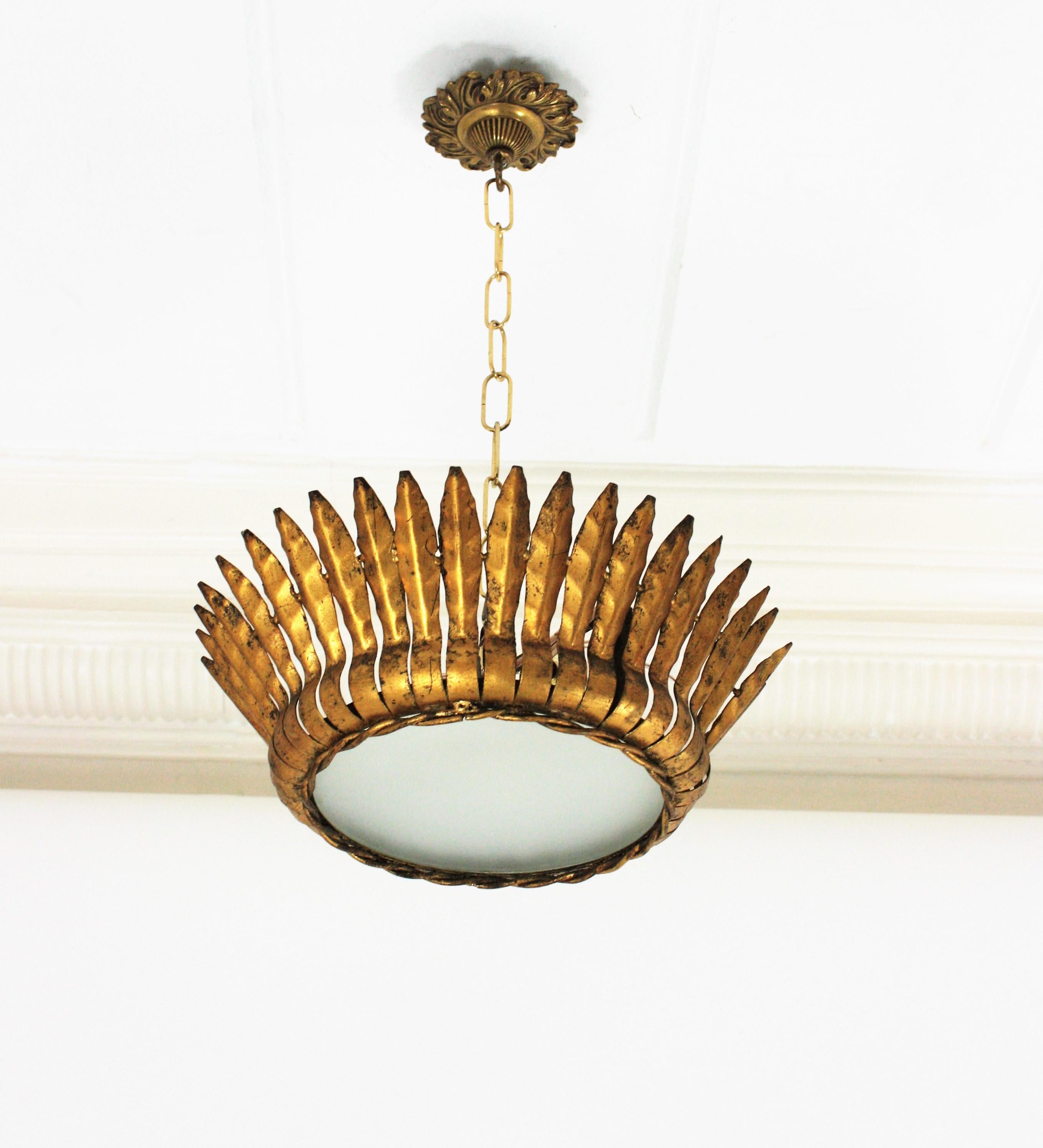 Pair of Mid-Century Modern gilt iron crown sunburst flush mounts or pendant with leaf motifs surrounding a central frosted glass diffuser, Spain, 1950s.
Handcrafted in hand-hammered iron with gold leaf finishing. They have a twisted iron rope