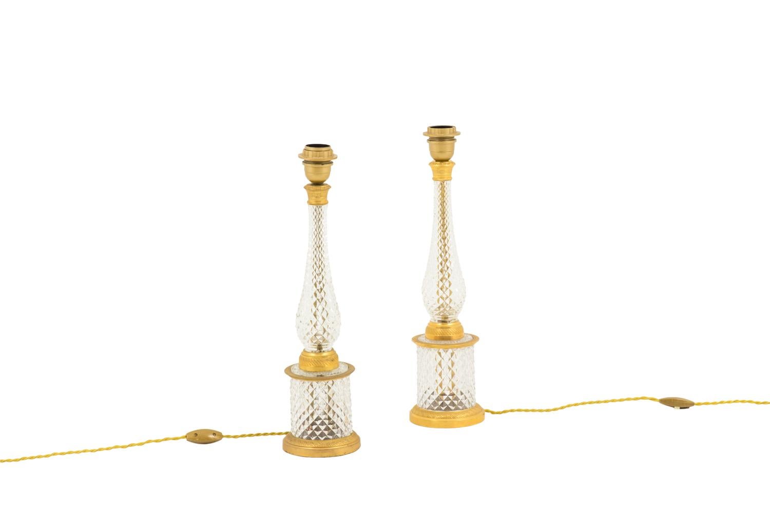 Pair of lamps in transparent crystal cut in diamond facets and gilt bronze mount.
Circular crystal base circled by gilt bronze, in the bottom with a decor of swirl and small flowers and a frieze of stylized leaves on the top. Baluster shaped crystal
