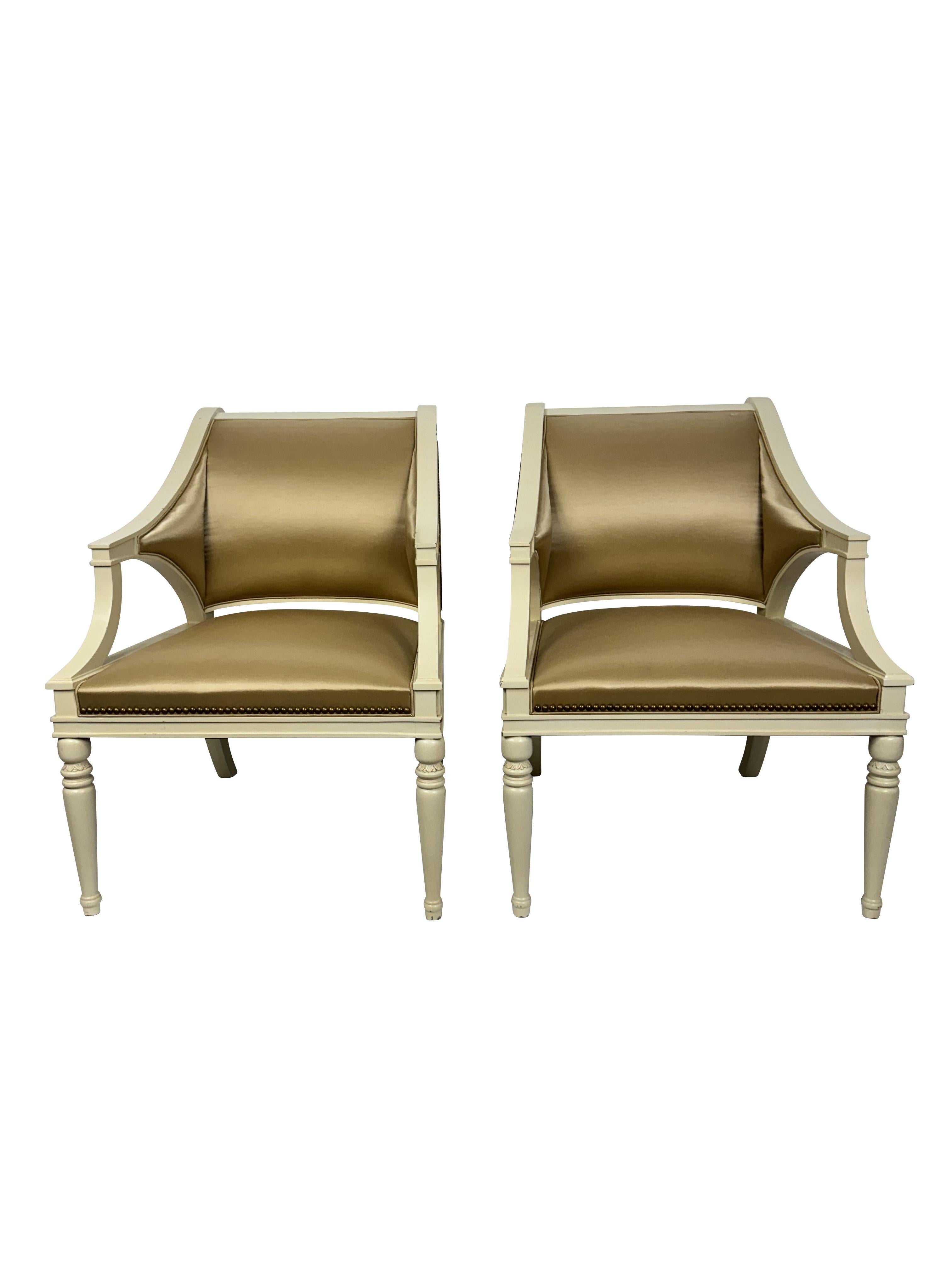 Paire de fauteuils décoratifs en soie champagne avec têtes de clous en laiton.  Grandes places assises confortables.  Peint en bois crème avec des pieds avant tournés et des pieds arrière de style Klimos,  Jolie sculpture sur les tabliers latéraux. 