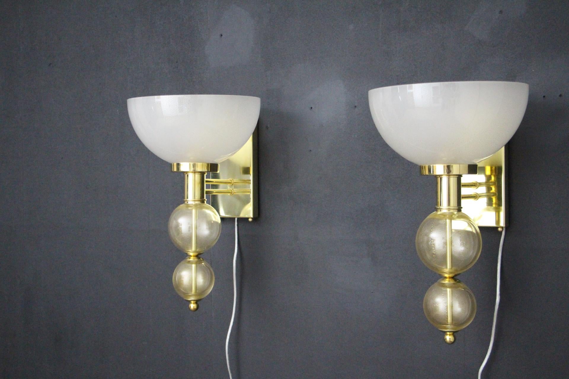 This magnificent pair of sconces features hand blown murano glass cup in a sweet ivory color with inclusions of golden bubbles inside the glass.They are sitting atop two gold spheres. Glass pieces are separated by polished brass fittings. Sconces
