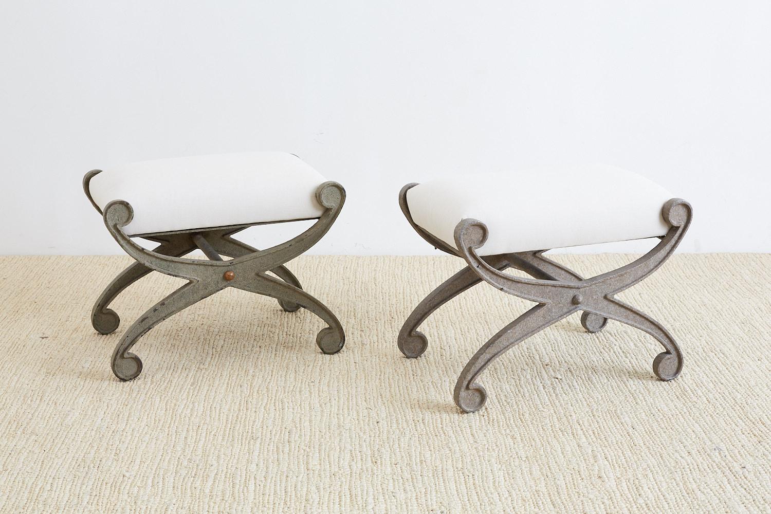 Amazing pair of curule iron benches or stools having an x form. Features a heavy, solid iron base with a lovely distressed patina and new cream upholstery. Custom made by a foundry in Los Angeles, CA.