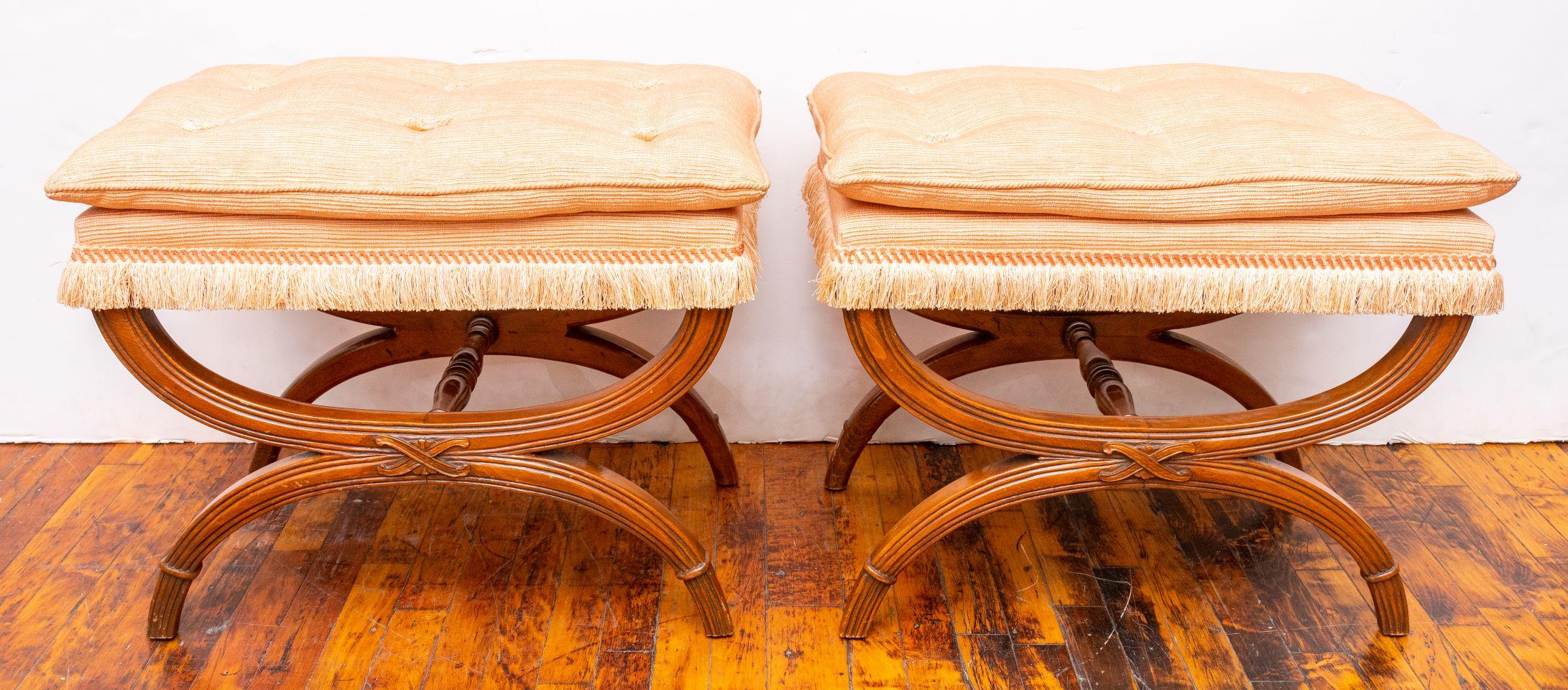 Pair of curule mahogany benches, upholstered in a peach fabric with matching fringe. Made in the 1970s. Very good vintage condition.