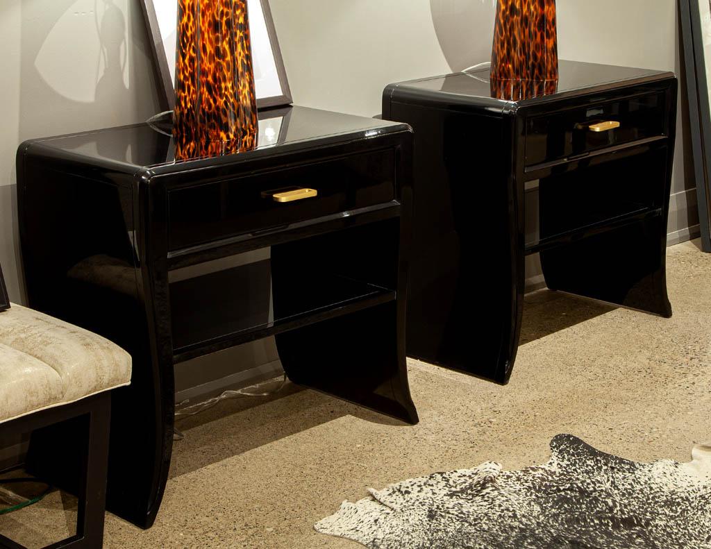 Pair of curved black modern end tables. Stunning curved waterfall design nightstand end tables with single top drawer and open shelf. Featuring sleek modern design in a high gloss hand polished black lacquered finish. Completed with modern brass