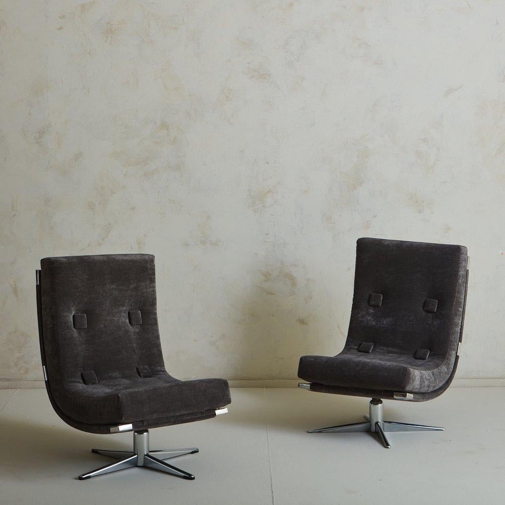 A pair of 1960s French swivel lounge chairs featuring dramatically curved seats with angular chrome hardware. These chairs have six oversized square button tufts and a sleek polished chrome x-base. They were freshly reupholstered in a beautiful dark
