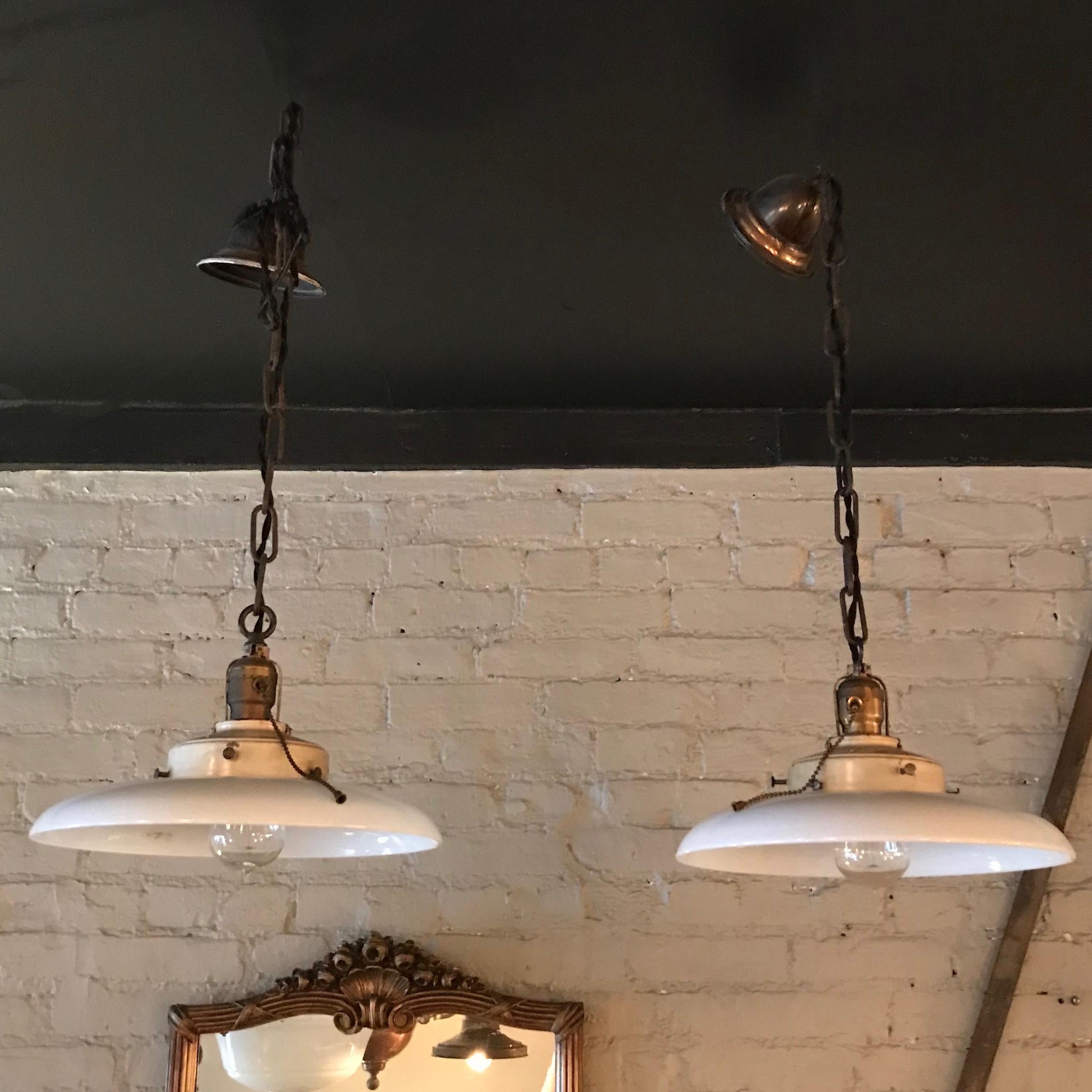Pair of industrial, factory pendant lights feature curved milk glass disc shades with baked enamel steel fitters on brass pull-chain sockets, brass chain, finished with brass canopies for the ceiling. The pendants are newly wired with braided black