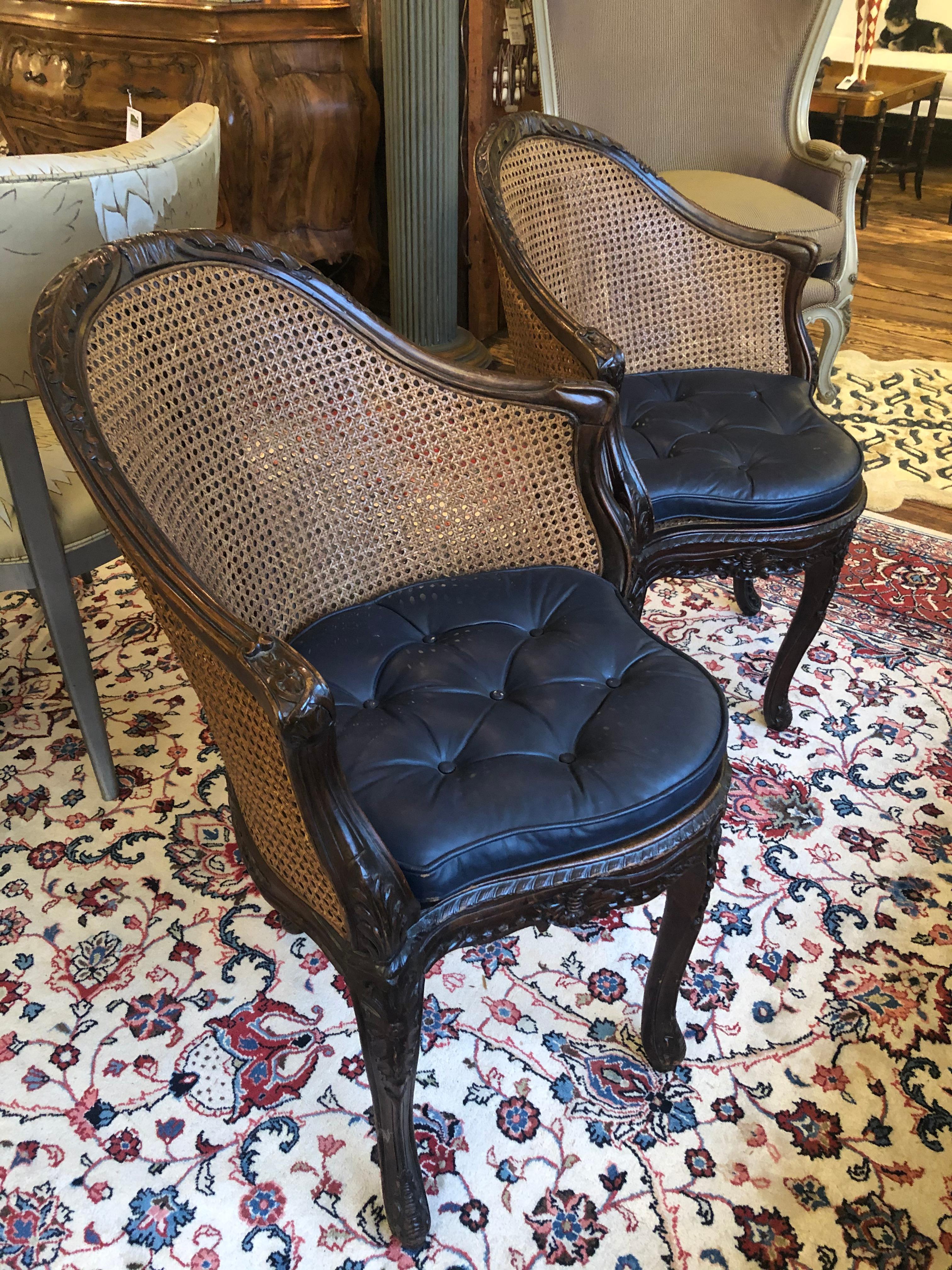 Wonderful antique pair of French carved walnut armchairs having rounded double caned backs, cabriole legs, caned seats and faux black leather cushions.