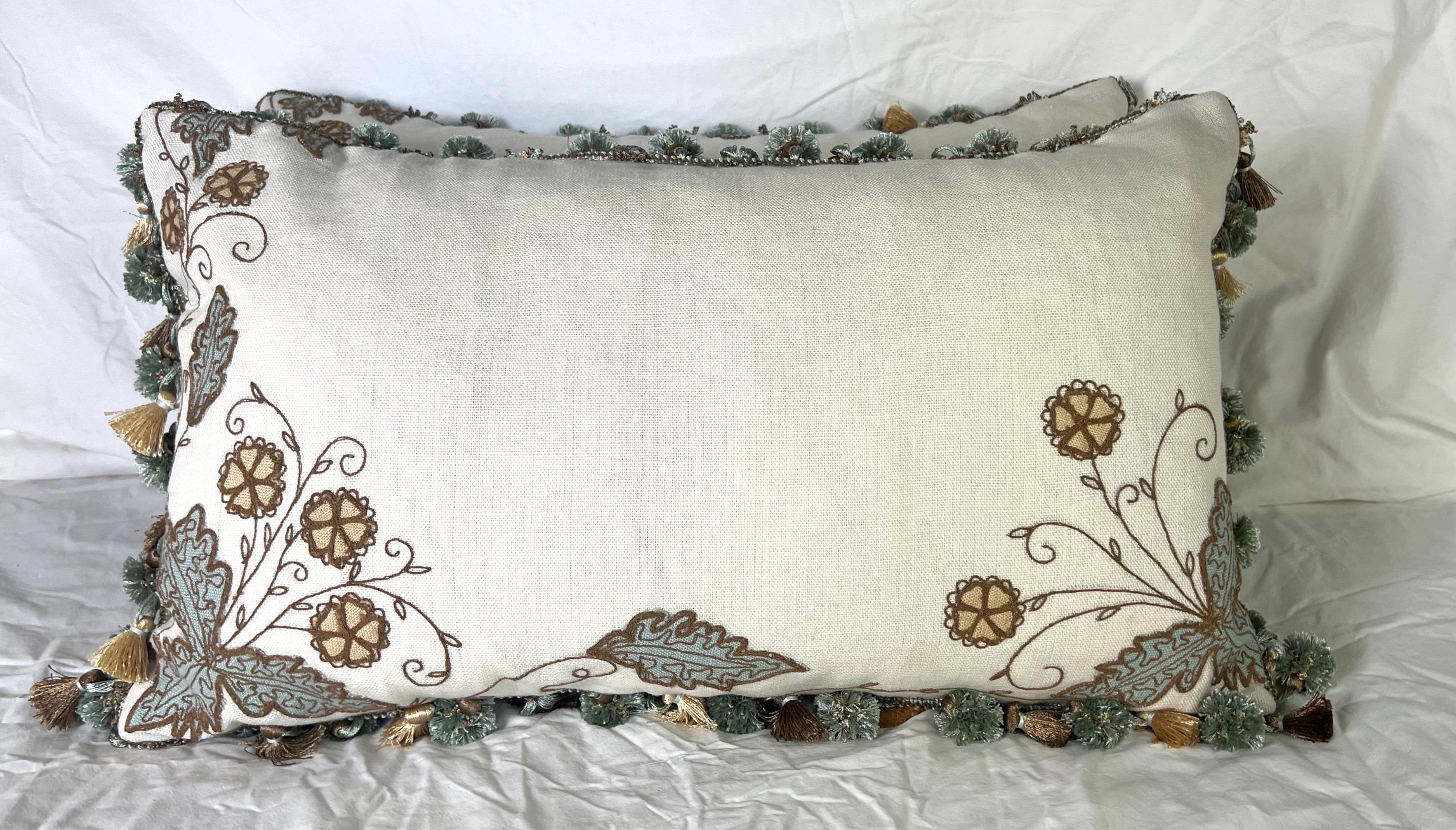 Par de almohadas personalizadas con un elegante lino bordado por El Palacio del Bordado.  El bordado presenta motivos florales en tonos terrosos, incluidos marrones y azules.  Los bordes de las almohadas están adornados con flecos decorativos de