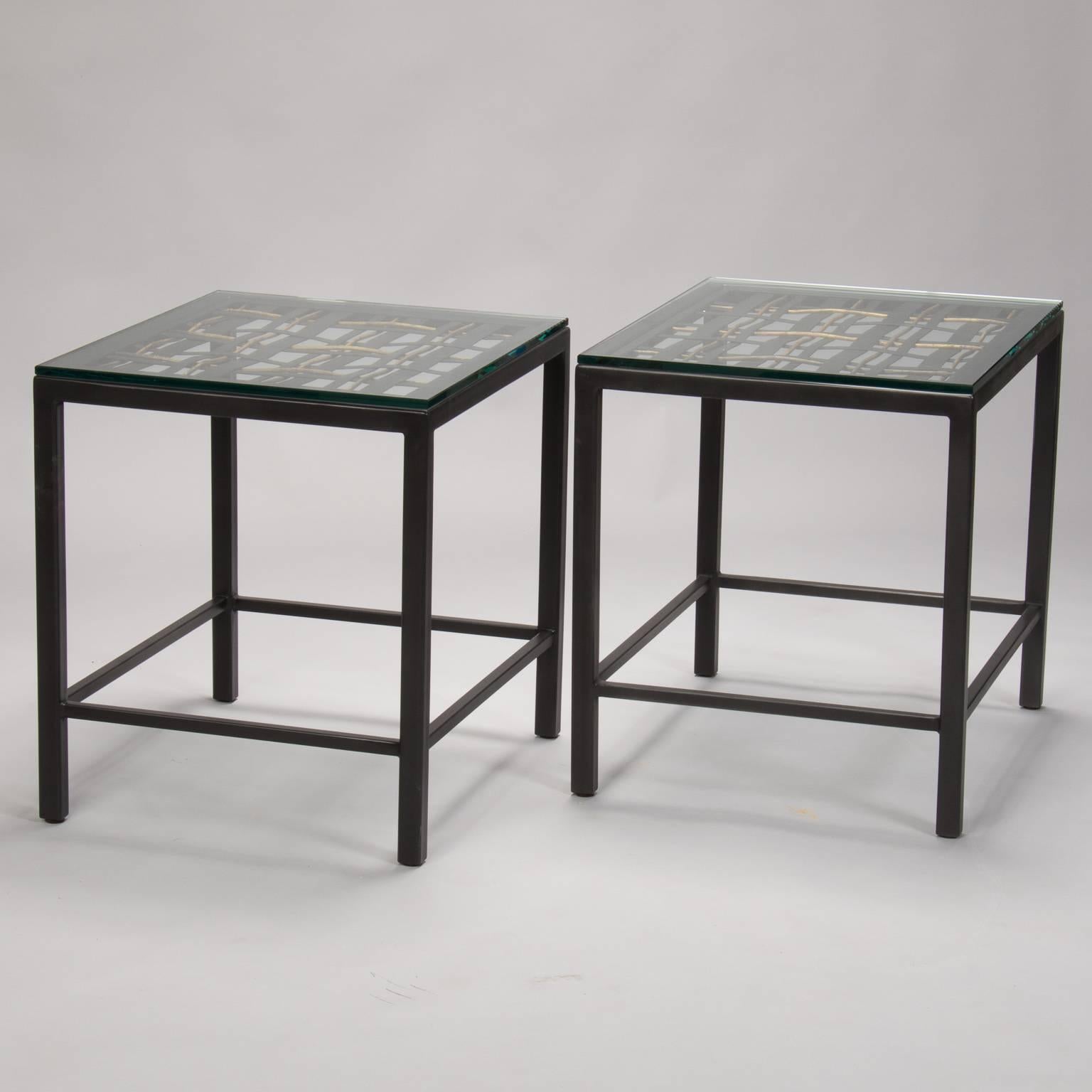 Decorative woven metal and iron fragment used as the top for this pair of end tables, circa 1940s. Wide flat metal pieces woven with narrower, gold colored iron strands are protected under a thick piece of glass and mounted in new, custom-made black