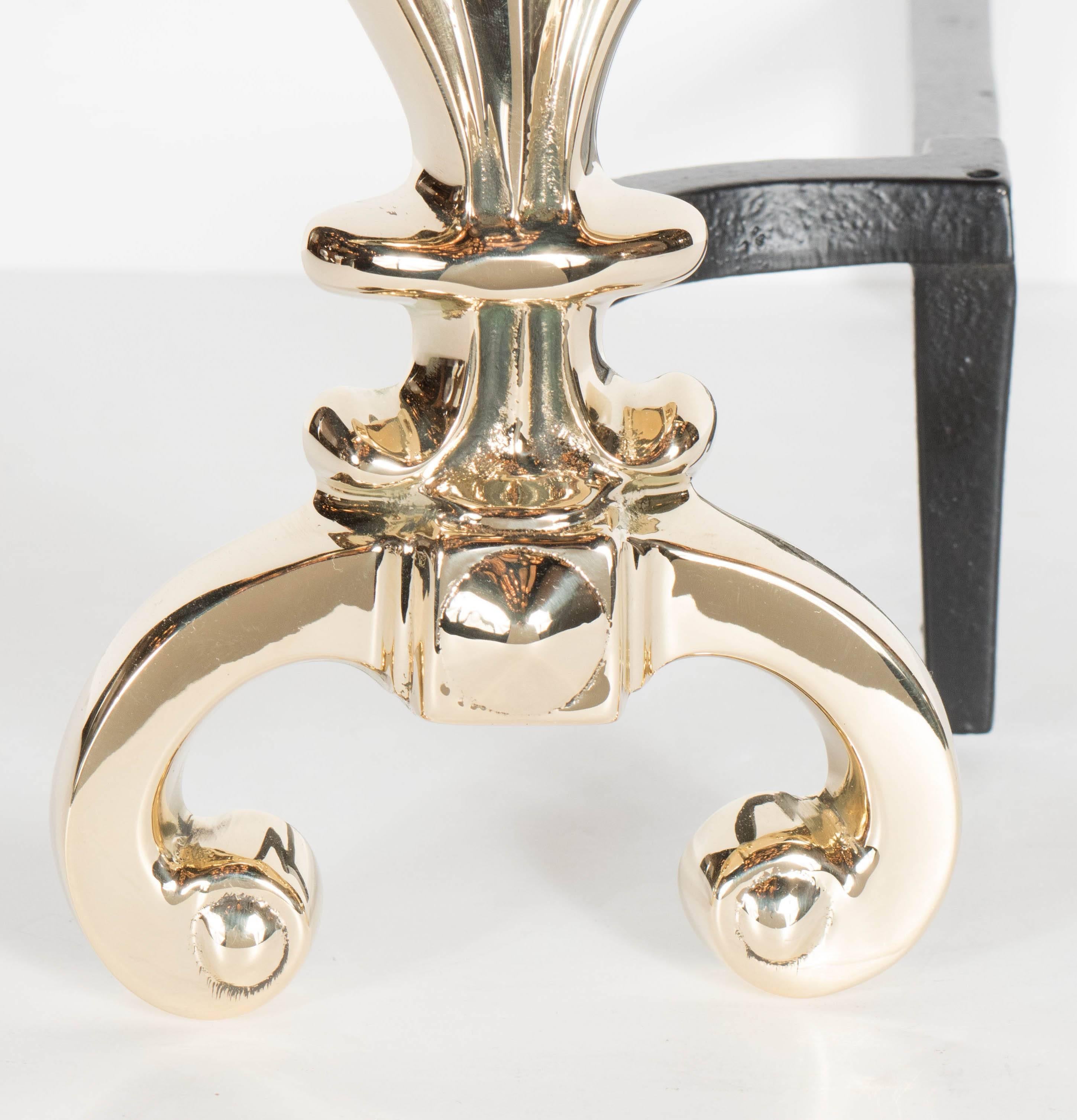 An elegant pair of custom Hollywood Regency style andirons feature a stylized fleur-de-lis design realized in polished brass. As this is a contemporary piece handcrafted by artisans from a centuries old forgery in Pennsylvania- they can be custom