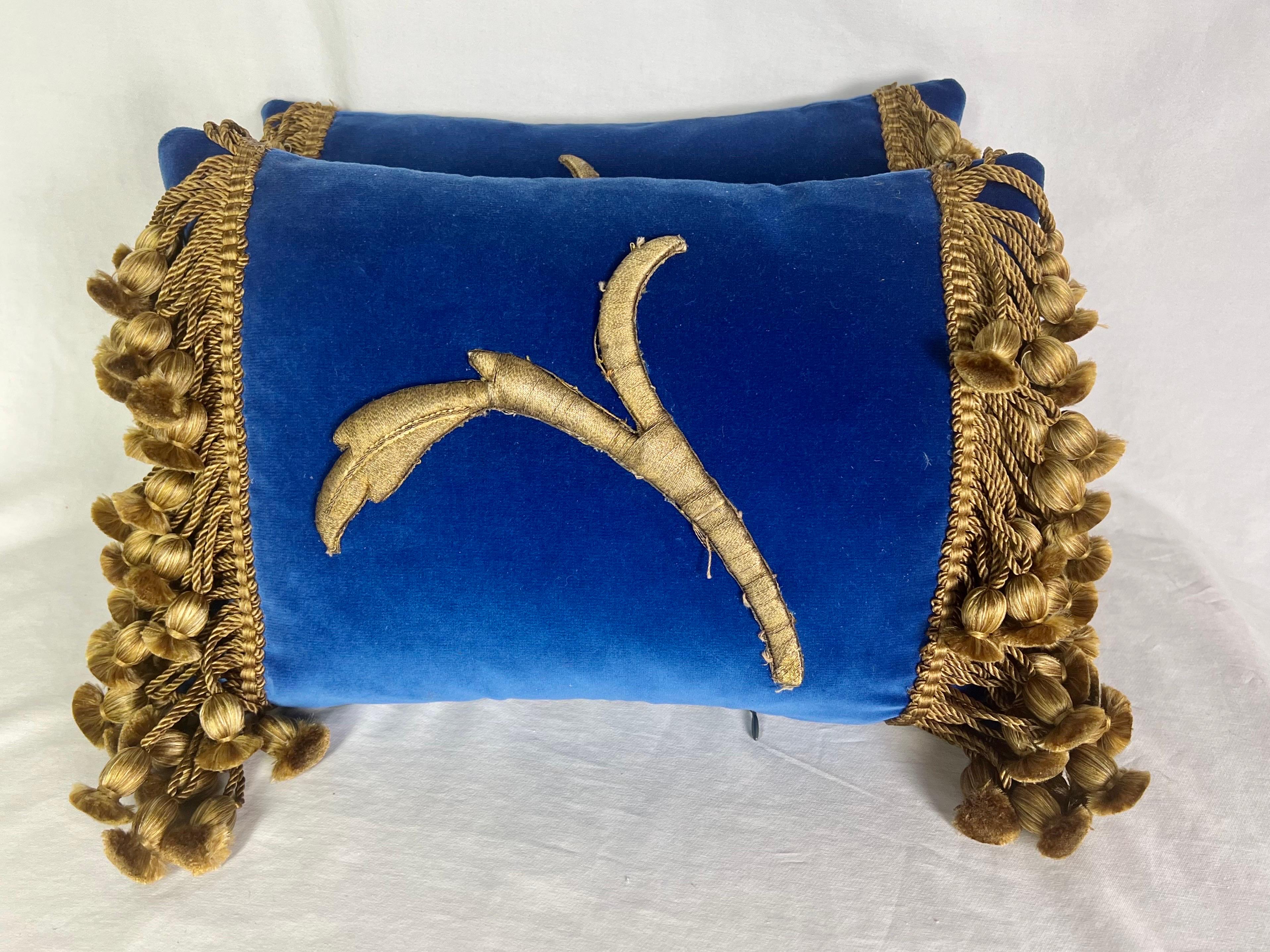 Pair of contemporary bark blue velvet pillows decorated with metallic thread acanthus leaf appliques and a golden colored tassel fringe on the ends.