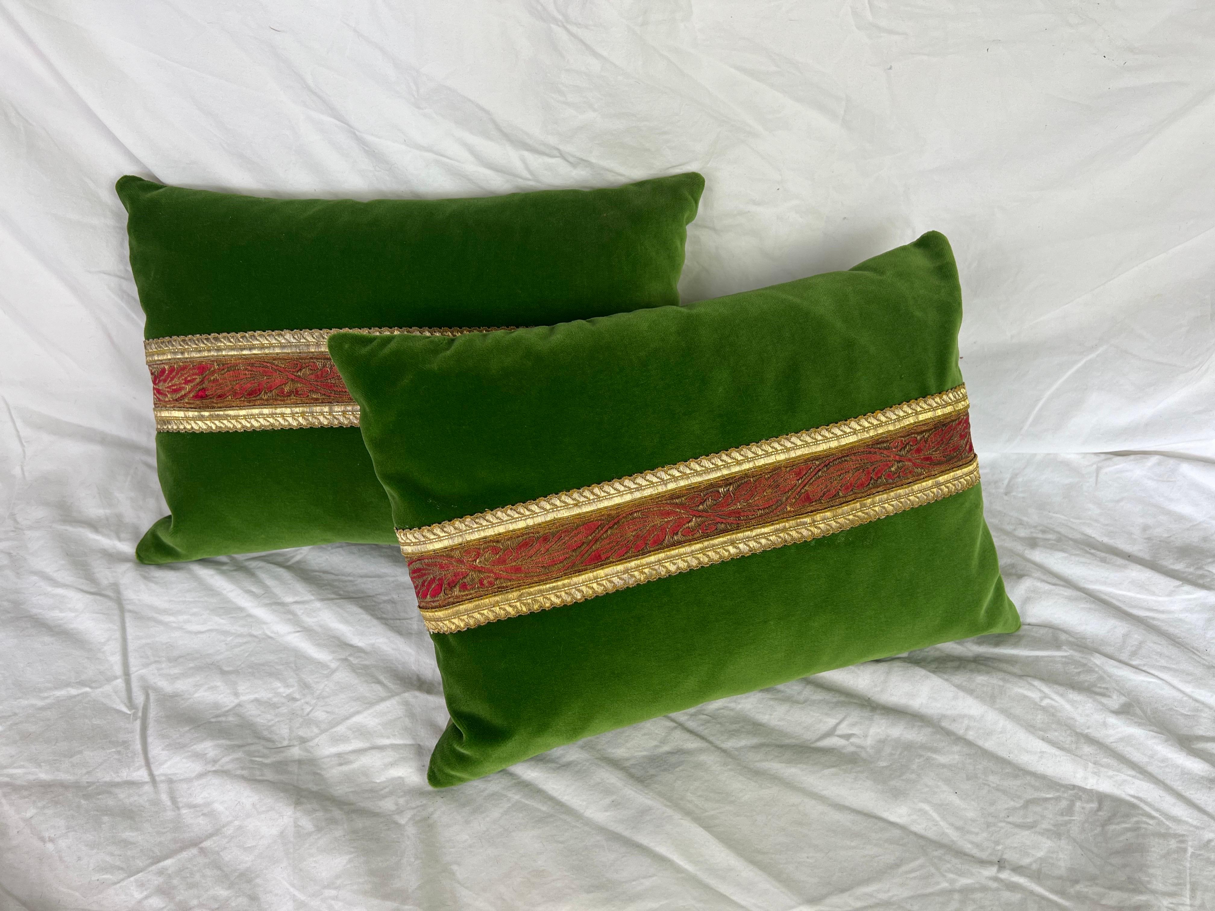 Coppia di cuscini personalizzati realizzati da MLA.  I cuscini sono realizzati in velluto di seta verde con un nastro metallico rosso/oro antico al centro. Il retro è di un verde coordinato.  Inserti in piuma, cerniere nascoste.