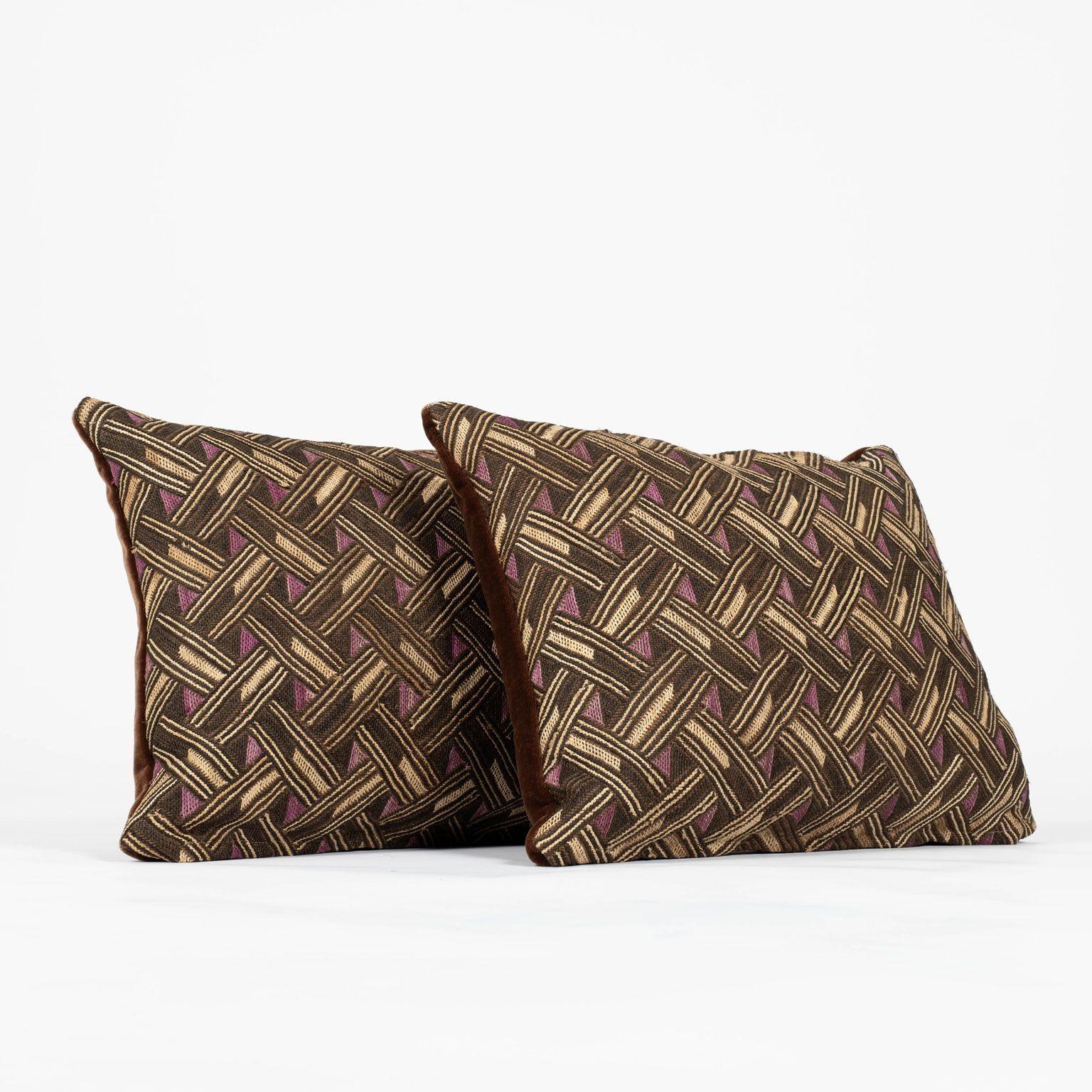 Pair of custom lumbar cushions from vintage African Kuba cloth. Hand-dyed raphia palm handwoven in a checkered pattern. Backed by brown velvet. Cushions nclude zip fasteners and feather inserts. Sold together priced $900 for the pair.