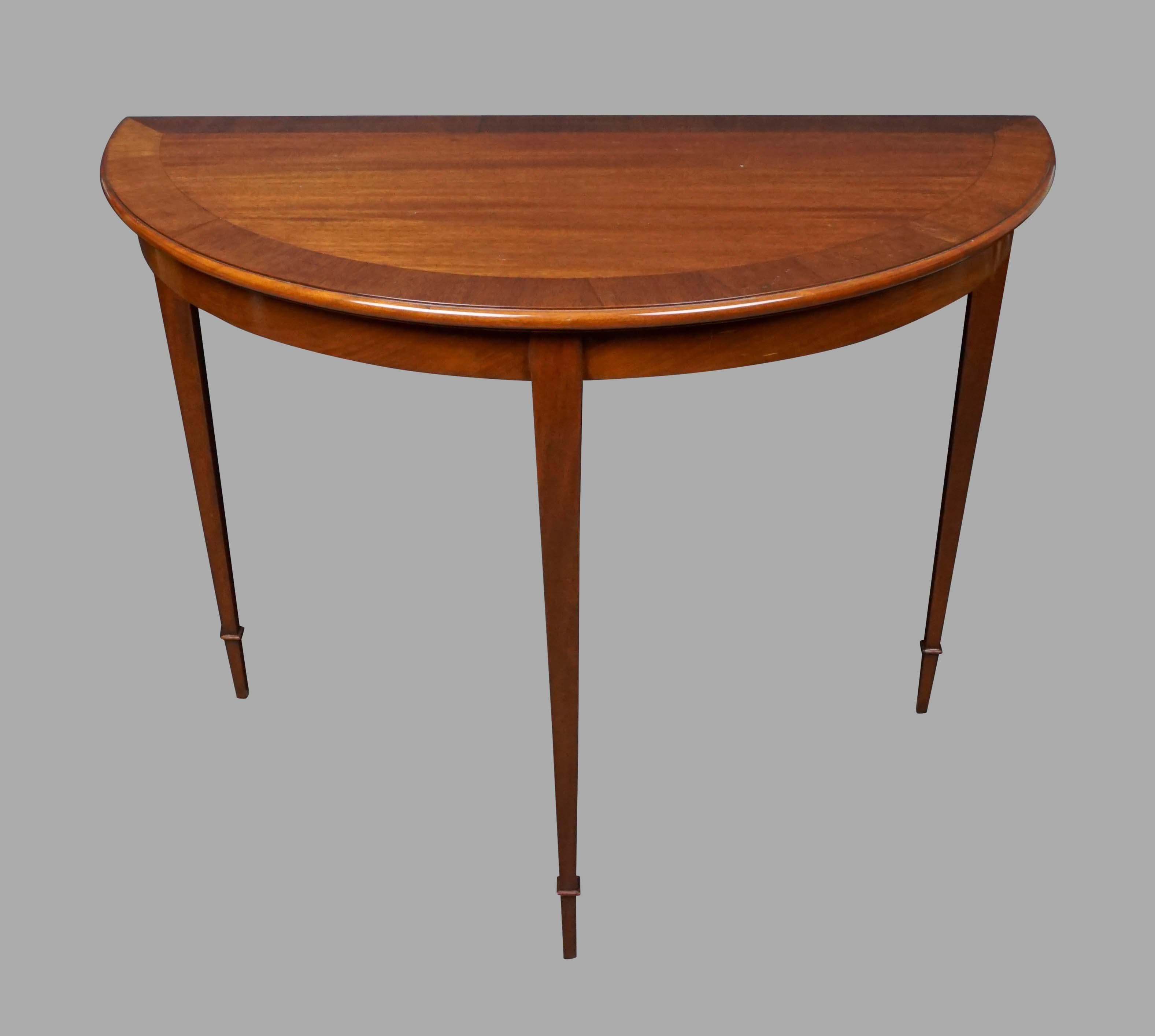 An attractive pair of mahogany demilune tables with crossbanded tops made and signed by well-known San Francisco cabinetmaker Claudio Mariani, each table with a crossbanded top supported by square tapering legs. An elegant reinterpretation of a