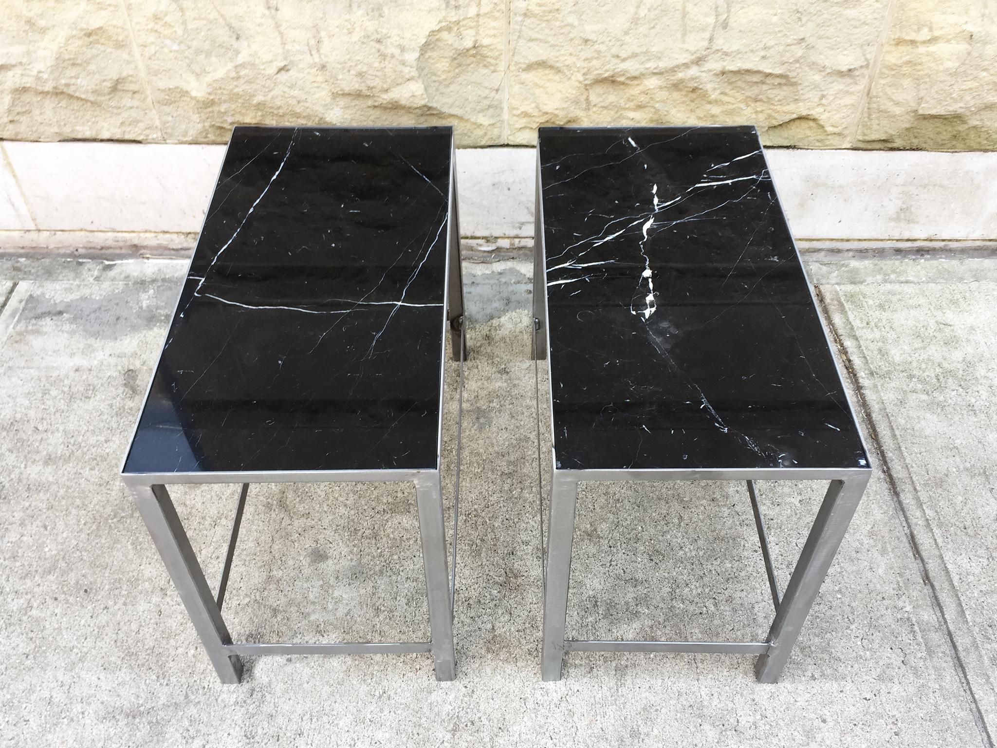 These remarkable custom end tables are newly handcrafted. They are comprised of black marble slabs and steel bases. The bases are soldered with lipped tops where the marble slabs fit securely, while the table's long, square legs are supported with