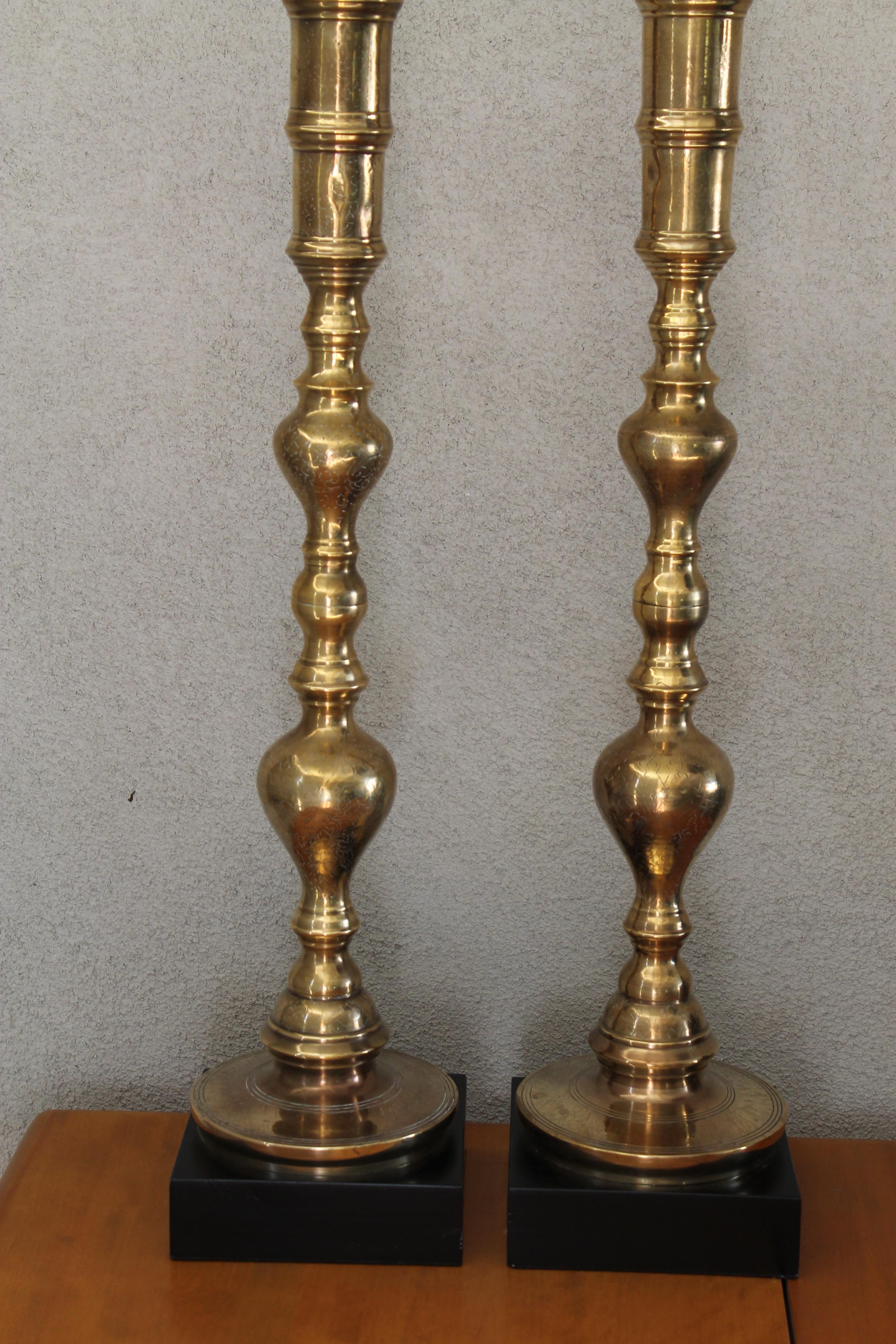 A matched pair of tall solid brass lamps with black painted wood bases. We took a pair of brass candlesticks and modified them to produce an elegant pair of brass lamps. Lamps measure 35