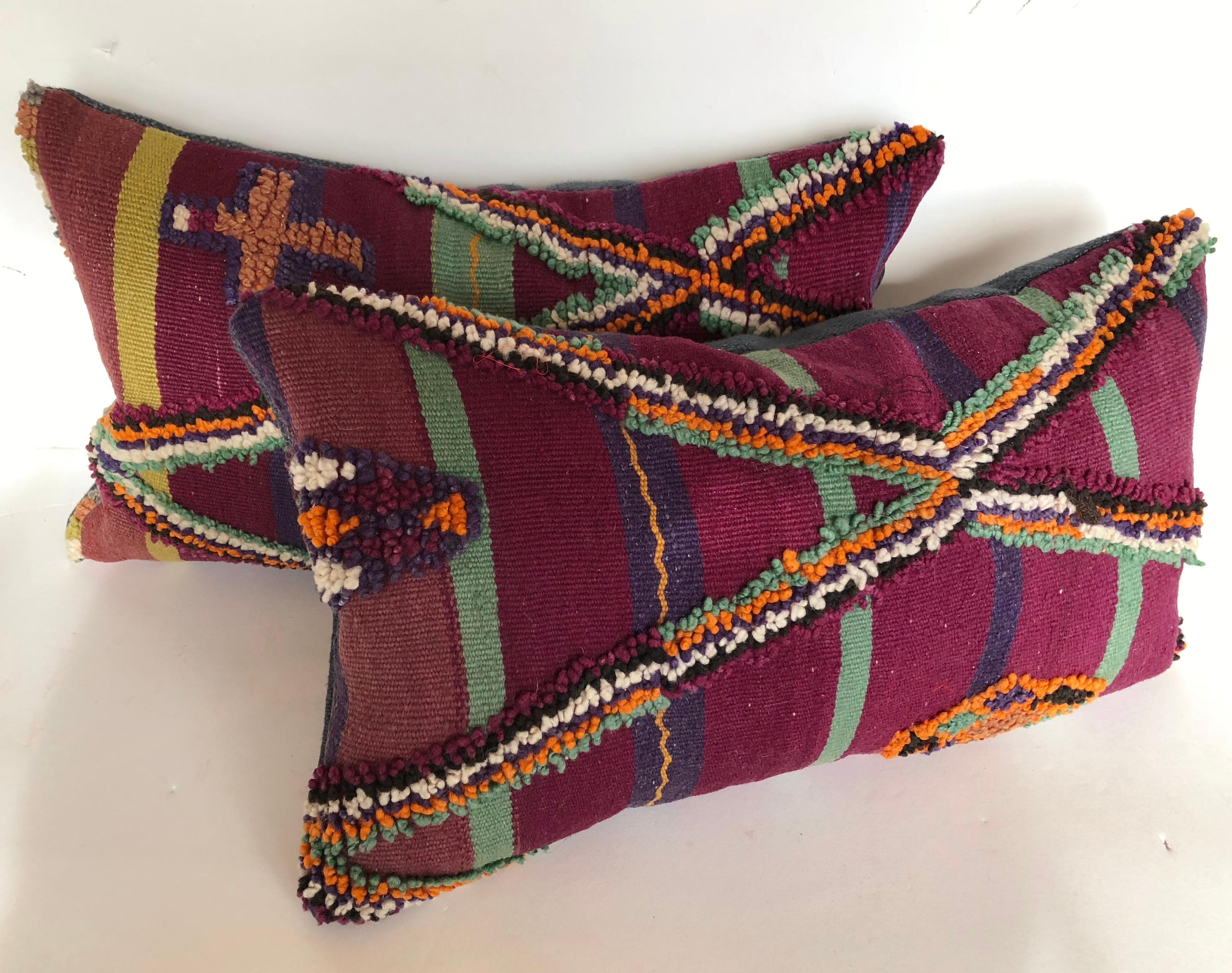 Pair of custom pillows cut from a vintage hand loomed wool Moroccan Berber rug from the Atlas Mountains. Wool is soft and lustrous with stripes and tufted tribal designs. Pillows are backed in a linen blend, filled with inserts of 50/50 down and