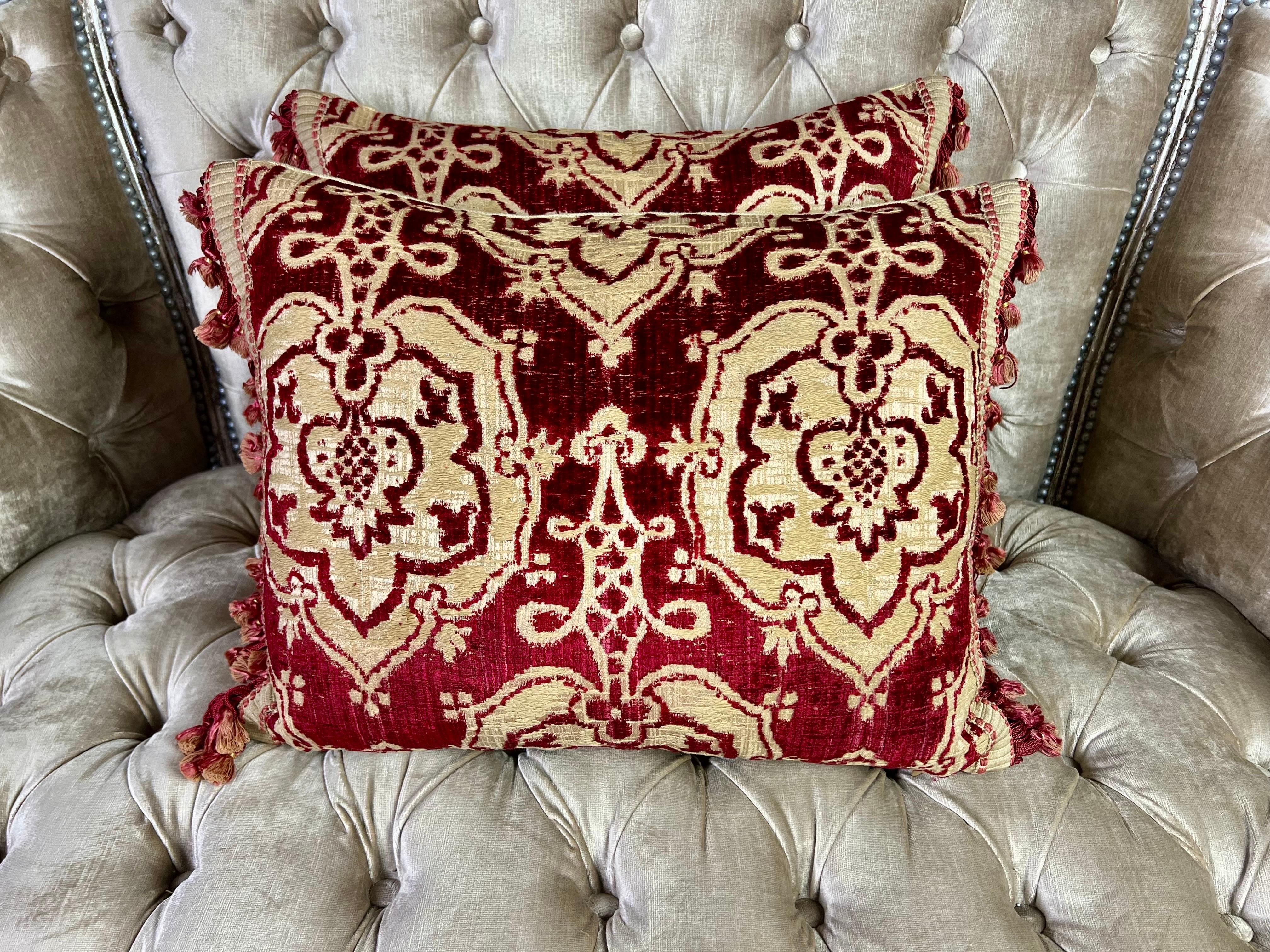 Pair of custom pillows made with rare early 19th century velvet Brocade in a crimson and wheat coloration.  Antique tassel trim at sides of pillows.  Linen backs and down filled inserts add to the luxurious pillows.