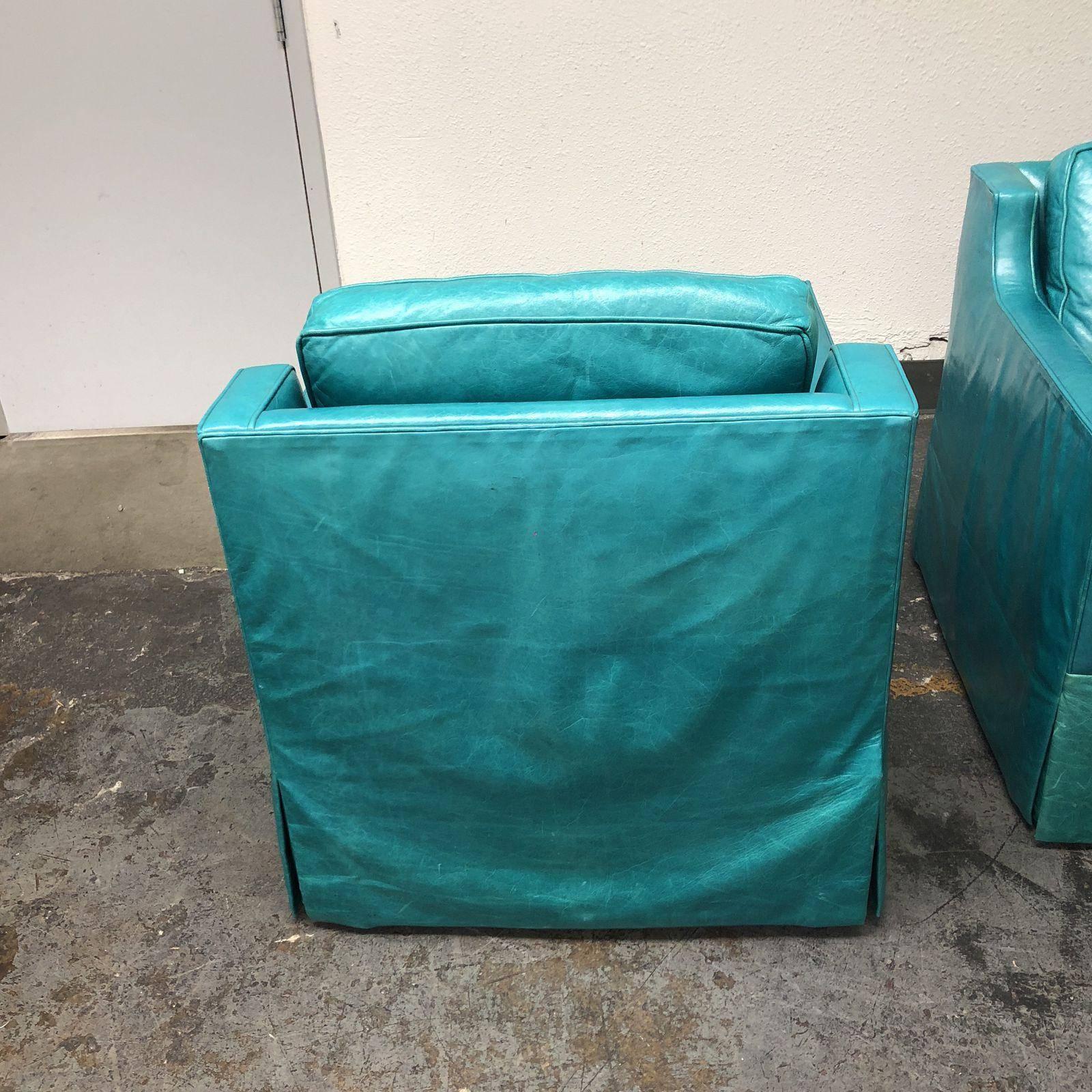 A pair of custom swivel leather arm chairs. Upholstered in a beautiful turquoise leather. The frame has slope arms with a leather skirt. The seat and back cushion are removable. The leather shows natural distress which creates a classic and