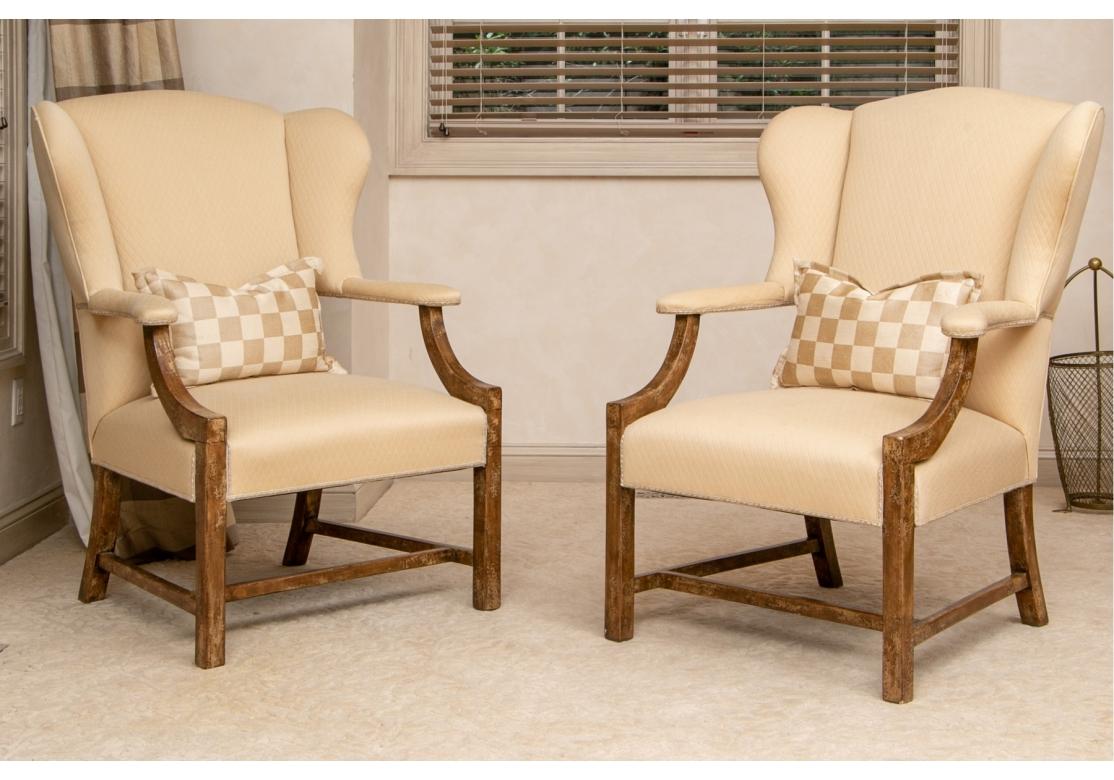 Pair of wing chairs in custom upholstered diamond form quilted fabric with contrasting lumbar pillows. The frames appear to be naturally distressed with a fine patina. The wing chairs with covered arms conjoined with sloping frame, stretcher base