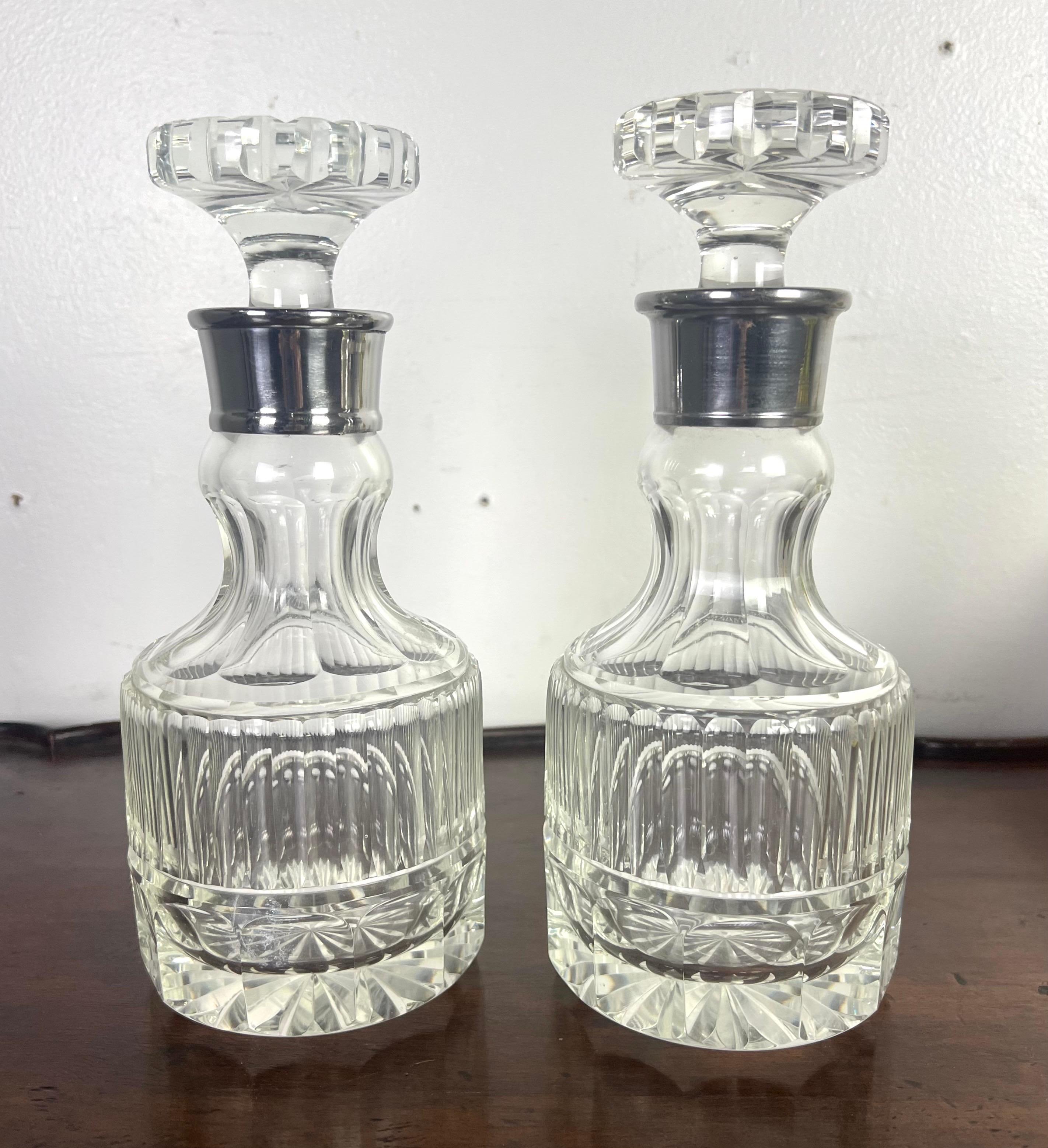 Pareja de elegantes decantadores de cristal con intrincados motivos tallados.  El diseño incluye una base facetada, detalles estriados verticales en la parte central y un cuerpo acanalado y redondeado que se estrecha hacia el cuello.  Cada