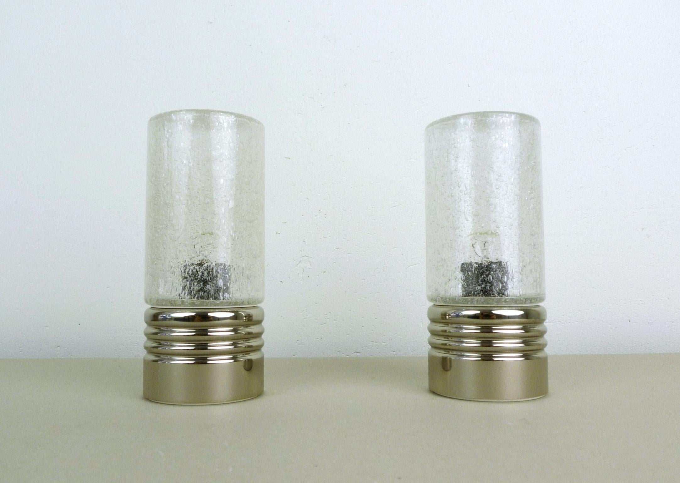 Pair of cylindrical table lamps with chromed metal stands and bubble glass shades from the 1960s. The shades create a sprinkled shadow on the wall. Each lamp is equipped with an E14 bulb socket. Both lamps are in very good condition.