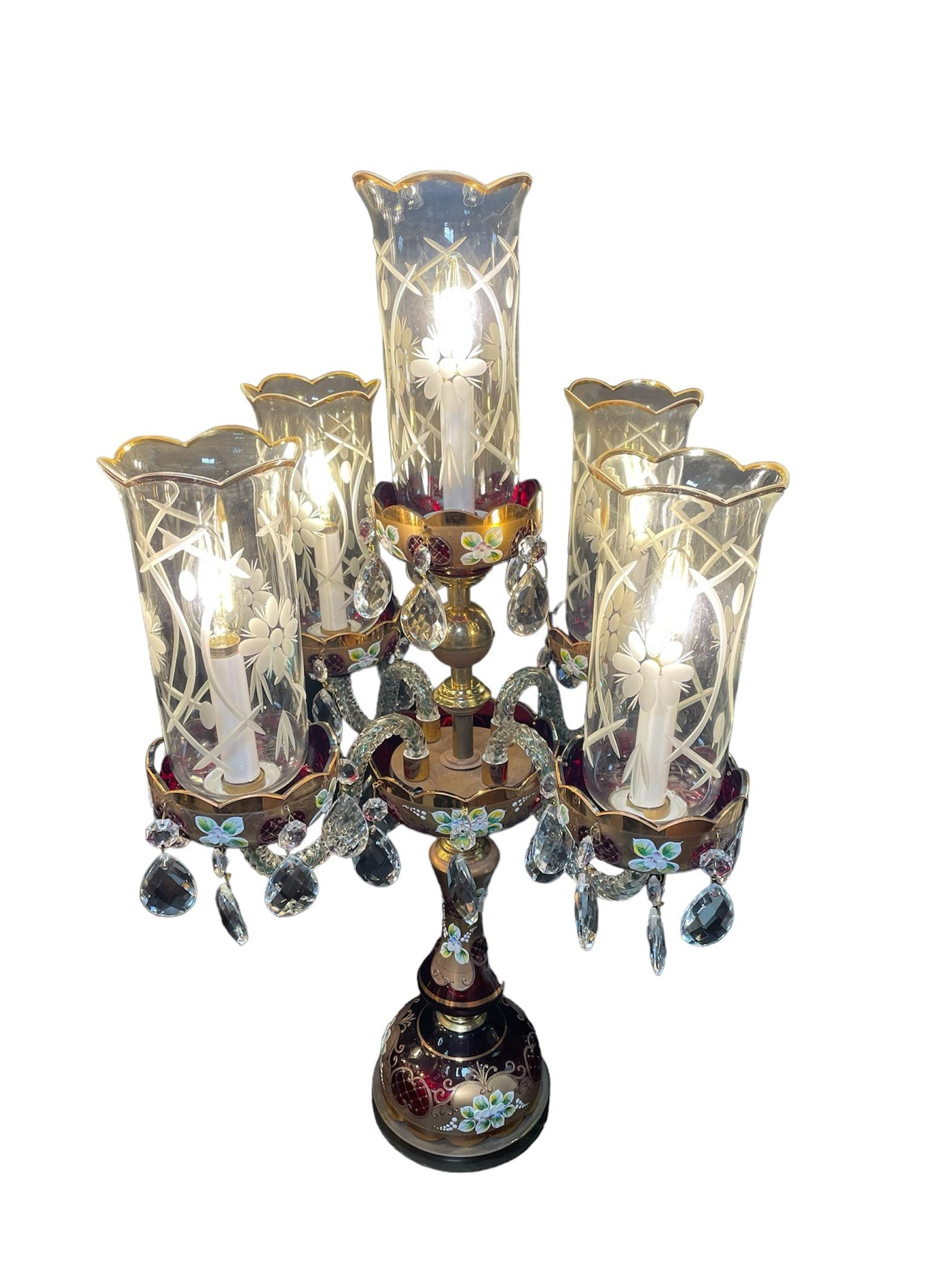 This is a Czechoslovakian Bohemian Glass Pair of Candelabras. It depicts an electrified pair of candelabras made of gilded ruby red glass decorated with enamel flowers and leaves. Both of them have five clear glass rope shaped arms ending in ruby