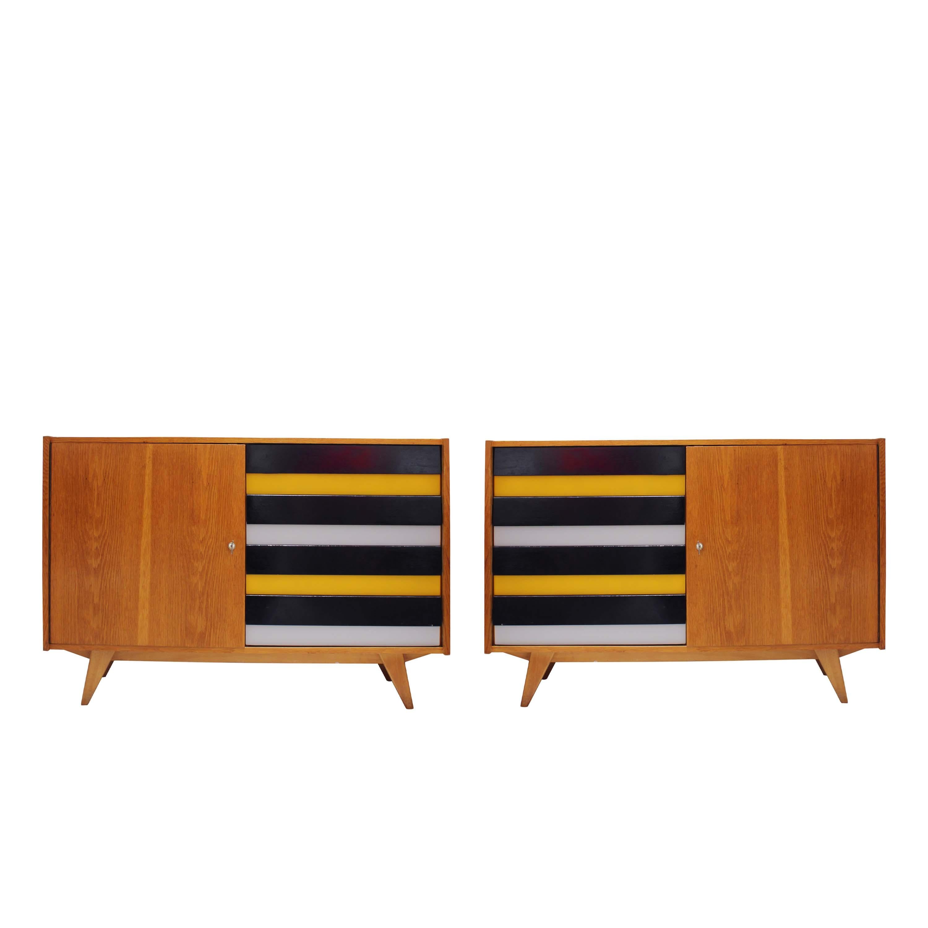 Striking pair of mid-century oak sideboards from 1960s Czechoslovakia. Each piece features four lacquered drawers in alternating black, yellow, and grey tones, placed on opposite sides, left in one, right in the other, creating a perfect visual and
