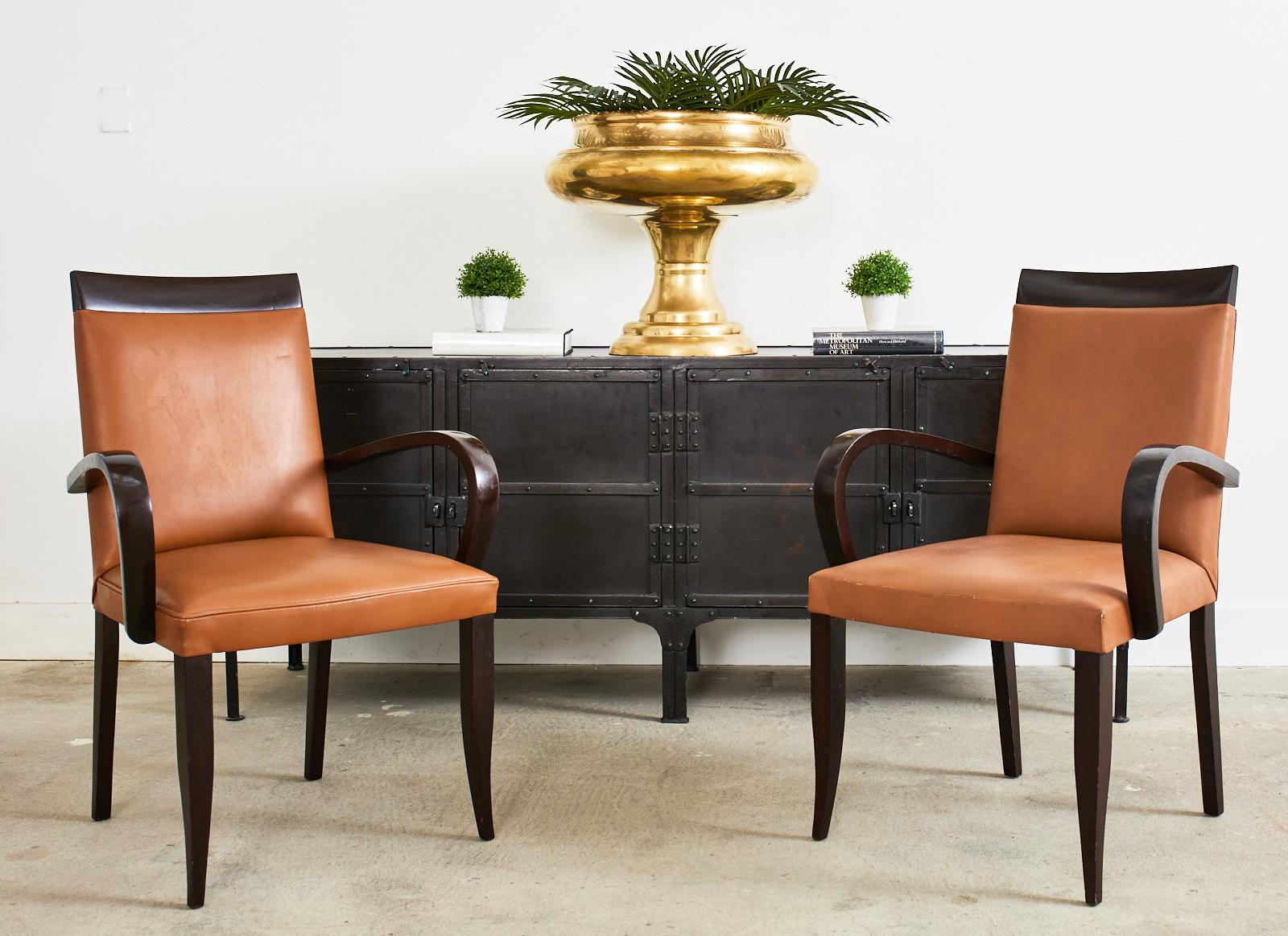 Dramatic pair of hardwood dining armchairs designed by Dakota Jackson known as PFM Royale chairs. The pair feature whimsical bowed arms conjoined to a generous seating area with cognac leather upholstery. Inspired by 1920s art deco the tops of the