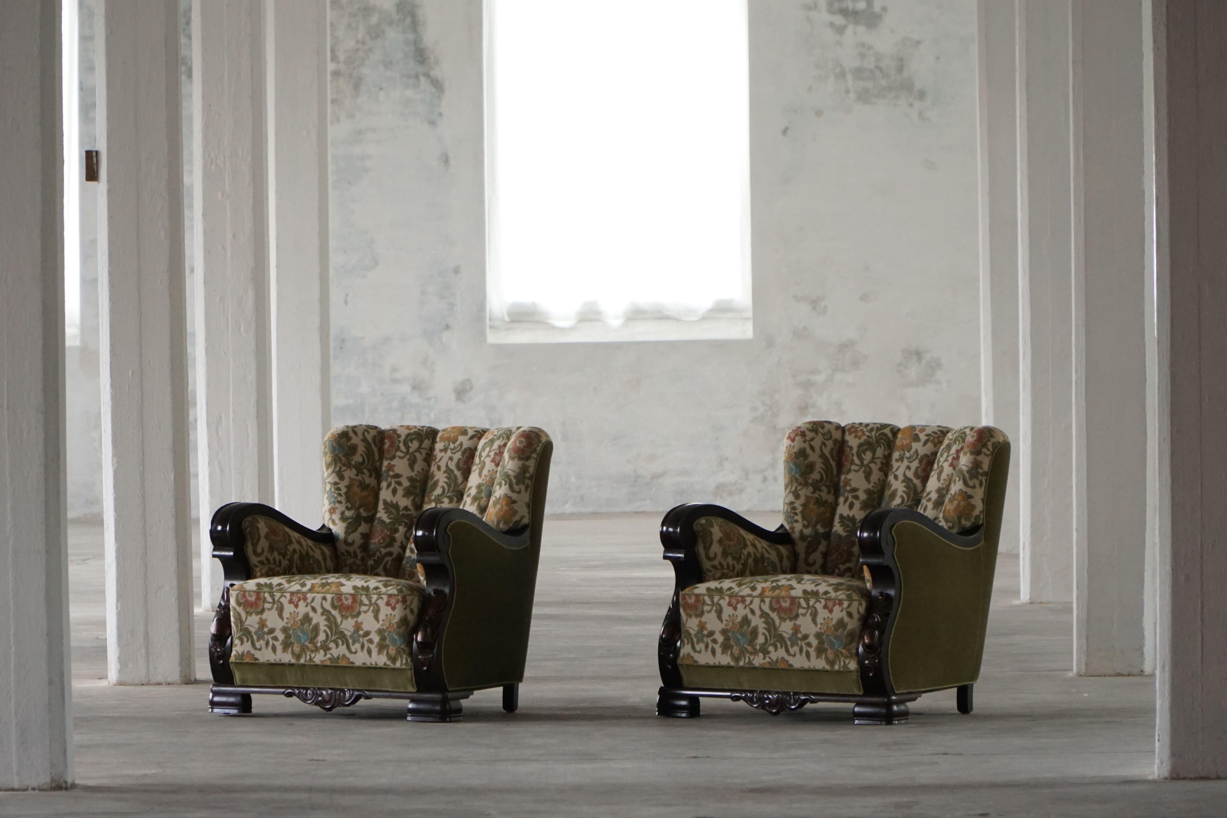 A pair of Danish lounge chairs from the 1920s, featuring a sculptural wood frame and generously upholstered in velour with a bold floral pattern. The upholstery combines beige and green tones with large, colorful flowers—giving of a vibrant yet
