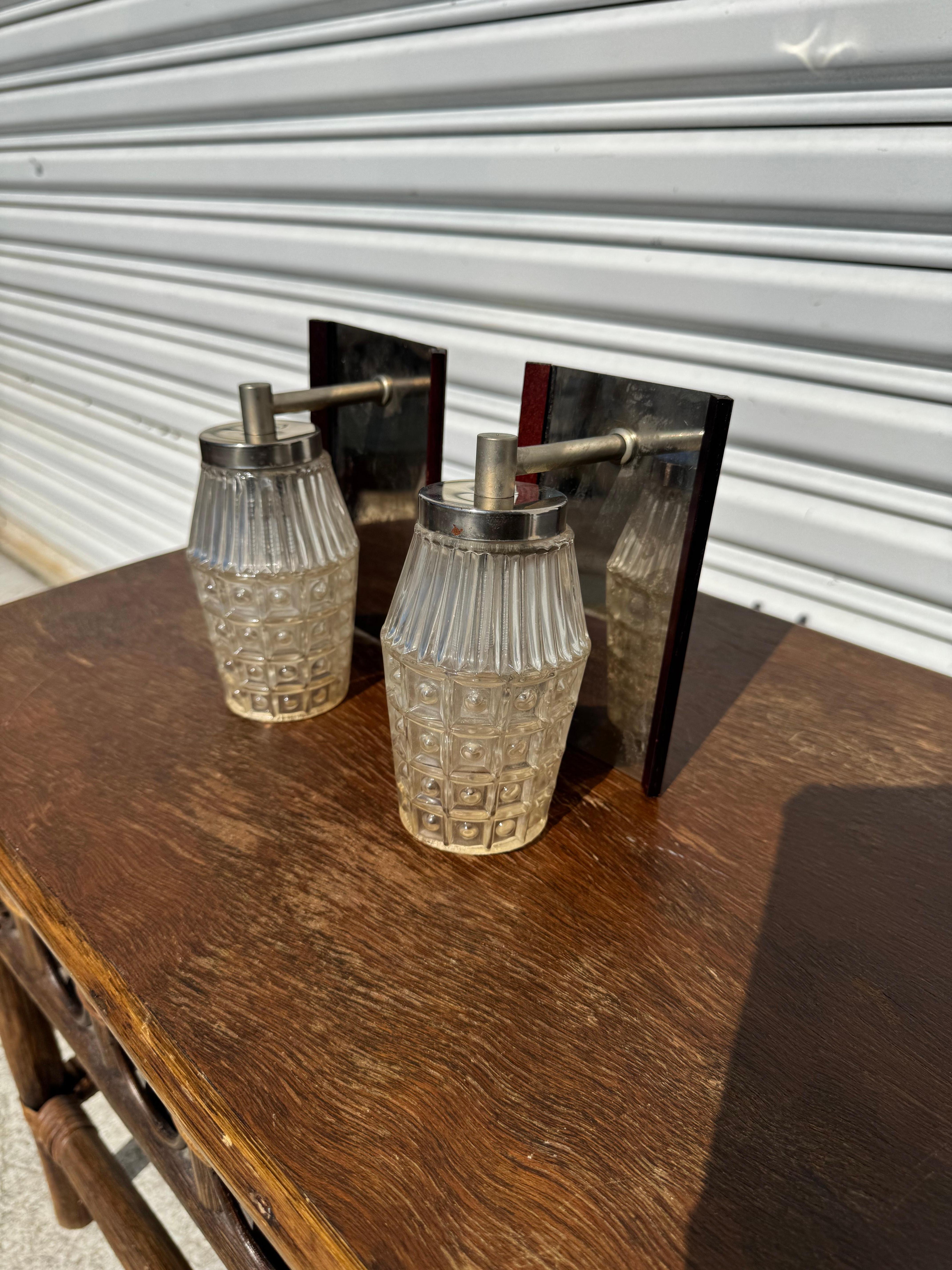 Cette paire d'appliques est composée de chrome, de garnitures en bois de rose et d'un abat-jour en verre taillé. Les lampes sont câblées 