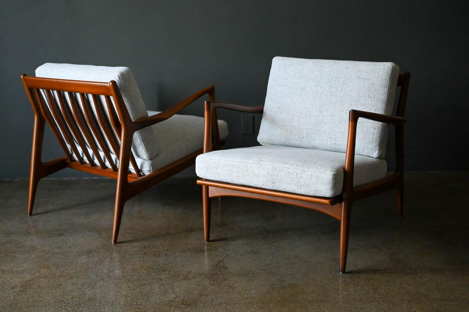 Pair of Danish lounge chairs by I. B. Kofod-Larsen for Selig, circa 1965. Beautiful walnut finish, professionally restored with new cushions and seat strapping. Classic spindle back design with sculpted armrests. New neutral grey/ivory tweed