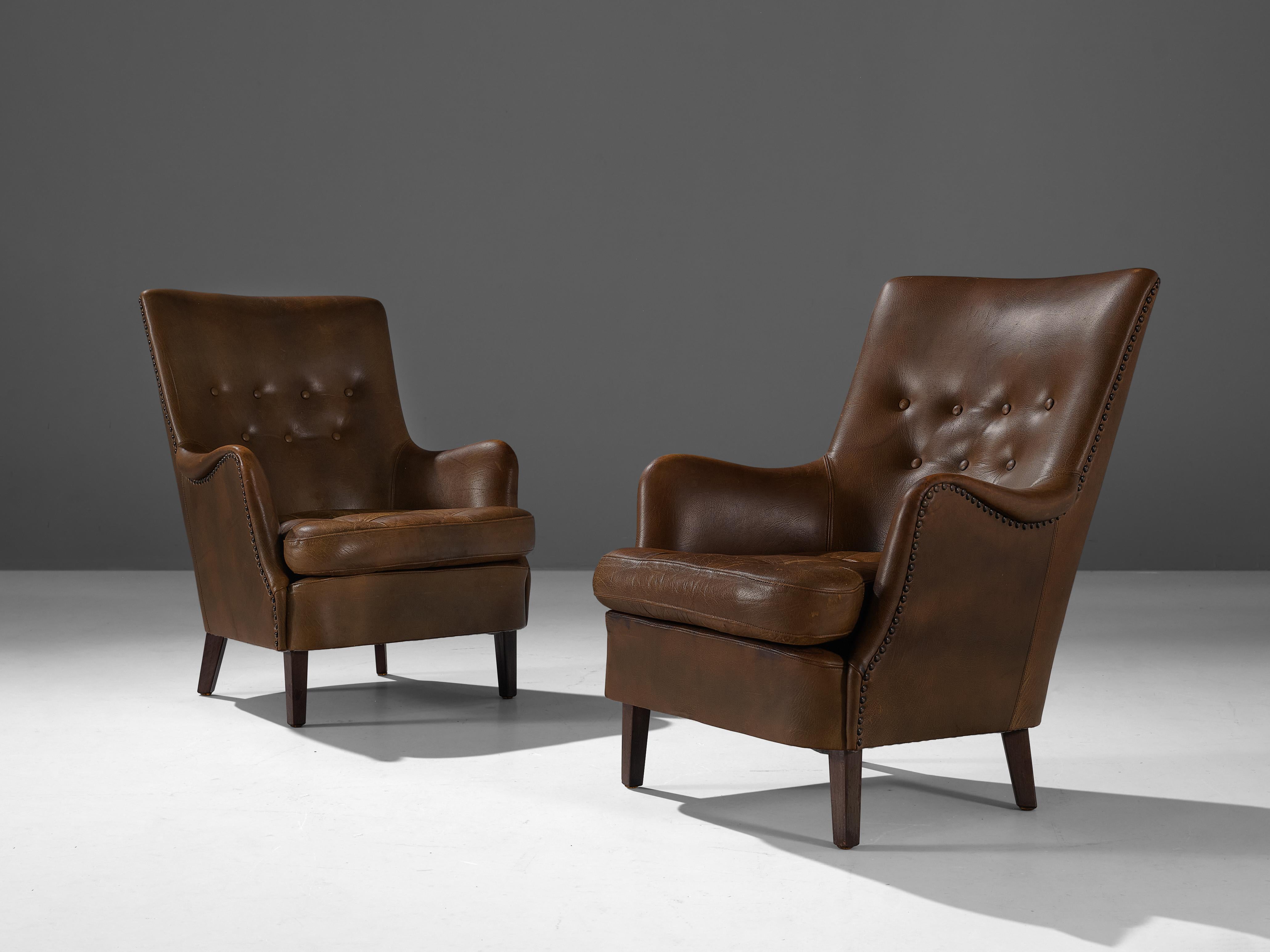 Lounge chairs, leather, beech, brass, Denmark, 1950s

Comfortable Danish lounge chairs in patinated brown leather. The leather is fixated to the chair with brass nails that contribute to the authentic look of the chair. Overall patina on the