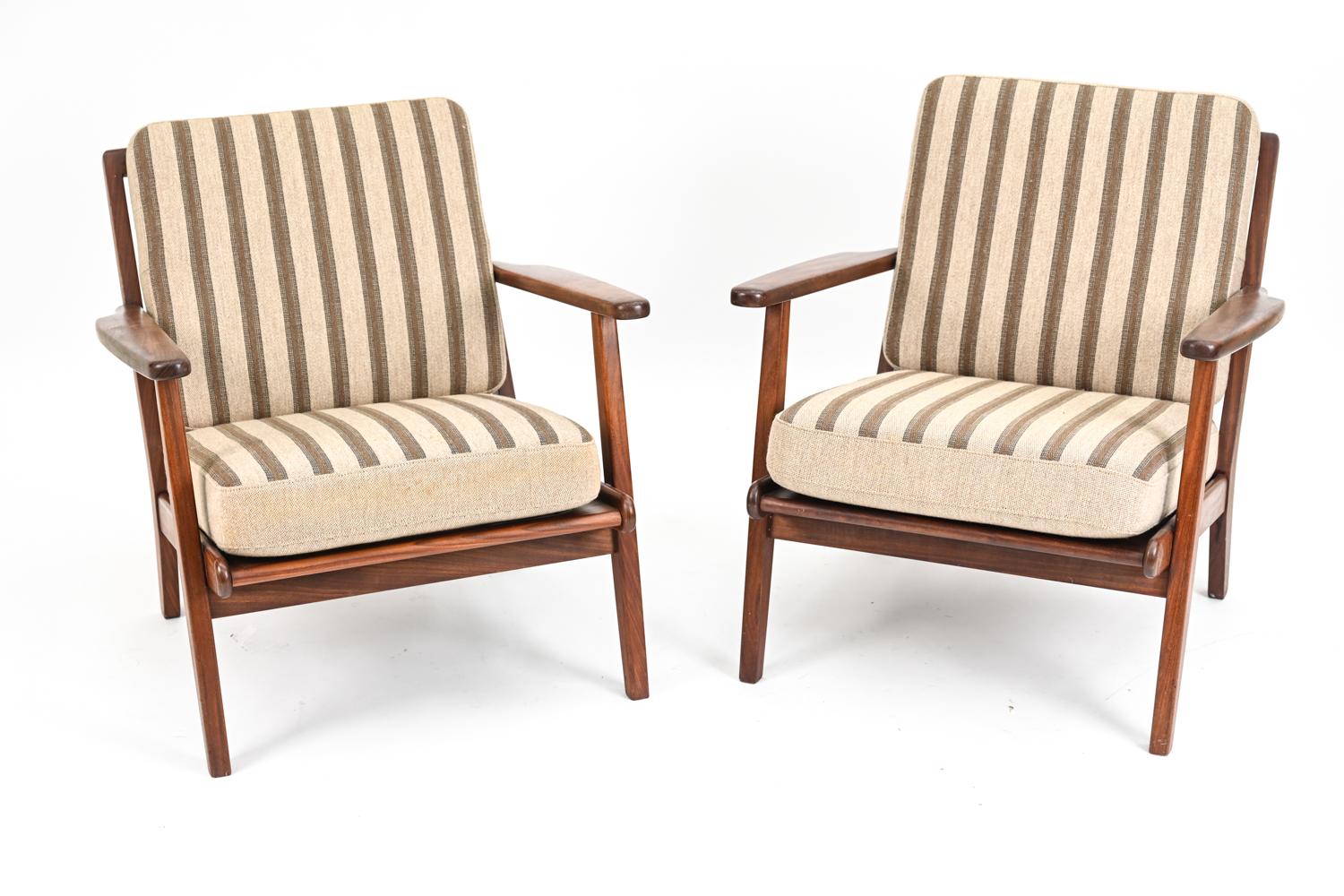 A handsome pair of Danish mid-century lounge chairs in the manner of Hans J. Wegner for GETAMA. These chairs feature dark stained teak frames and striped neutral wool cushions. 
No manufacturer's labels present.