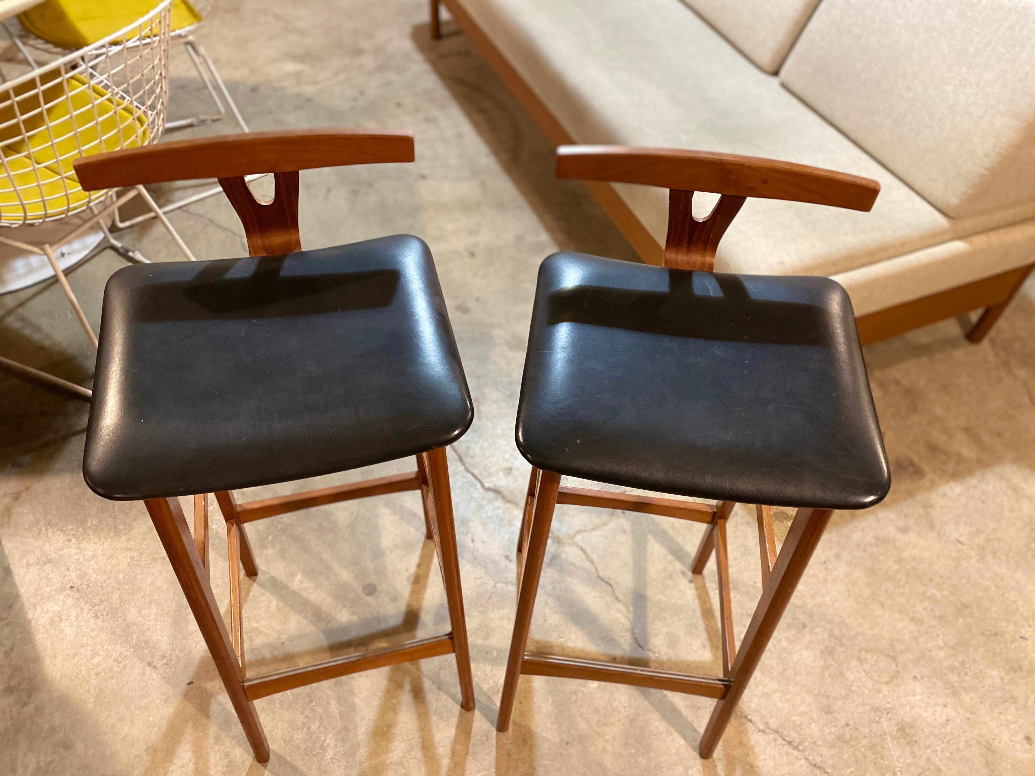 Pair of distinctive Danish barstools by Erik Buch for Dyrlund, Denmark circa 1960s. Barstools are made of teak, have a low t-back with leather seats, and are in great vintage condition. This pair of Classic Scandinavian Modern barstools are unique