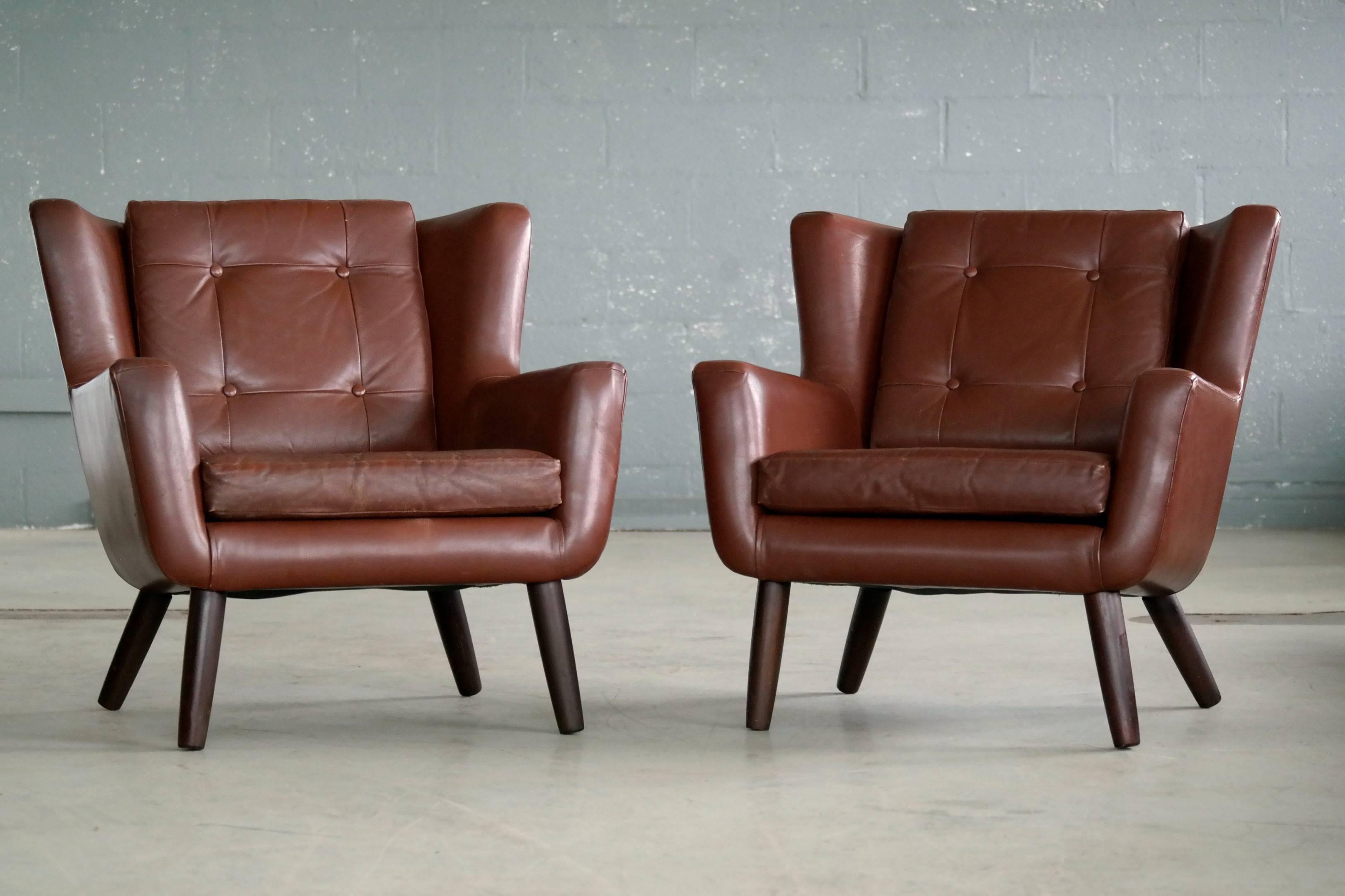 Pair of very charming easy chairs in a nice warm chestnut brown colored leather with tufted back and seat cushions raised on solid teak legs made in the 1960s by Skjold Sørensen of Denmark. Skjold Sørensen had a unique and very characteristic design