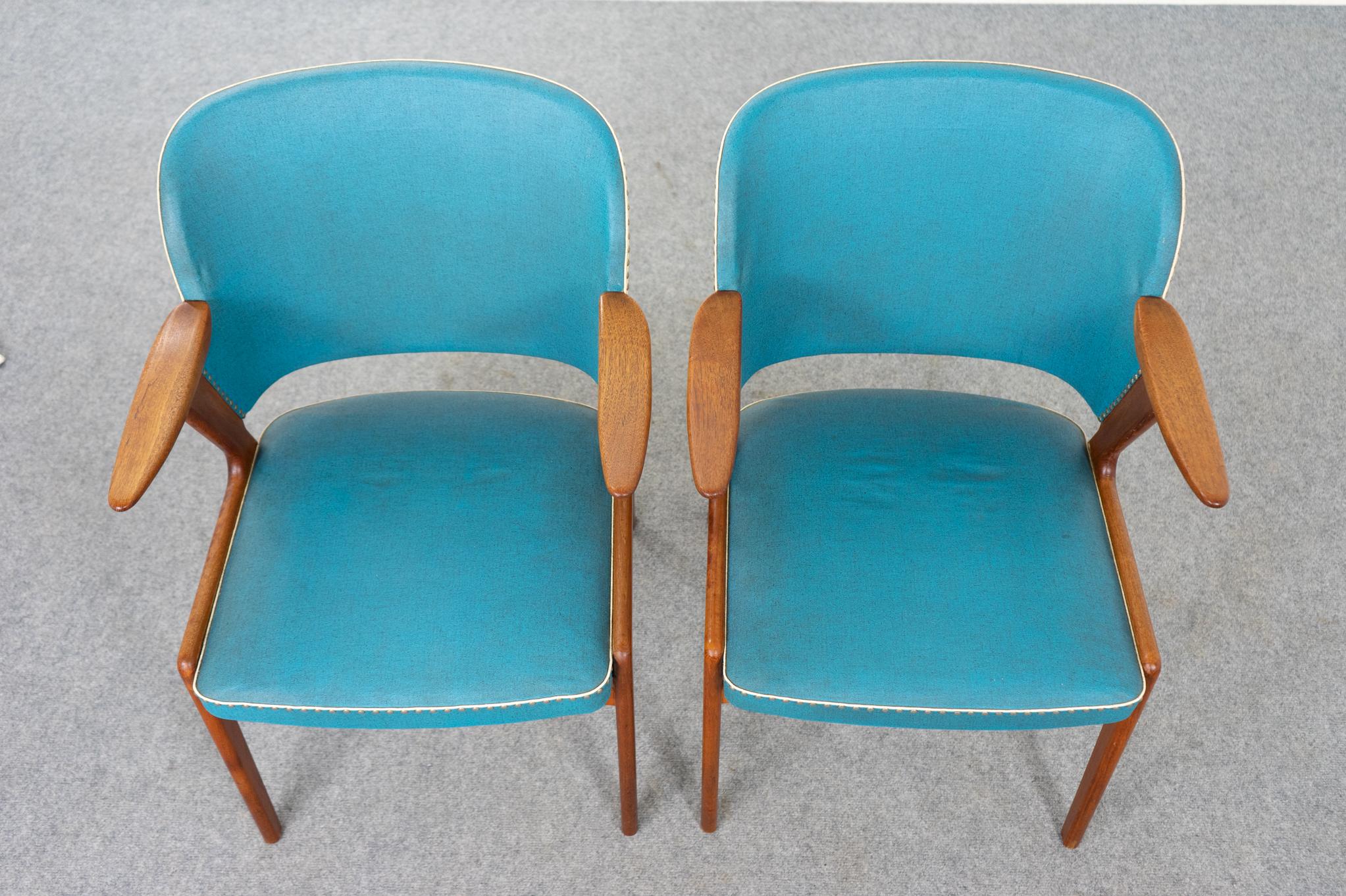 Pair of teak and vinyl Danish arm chairs, circa 1950's. Elegant frame with swooping arms is perfectly scaled for any room. Original contrasting teal and cream vinyl upholstery. Beautifully sculpted frame offers comfort without an imposing