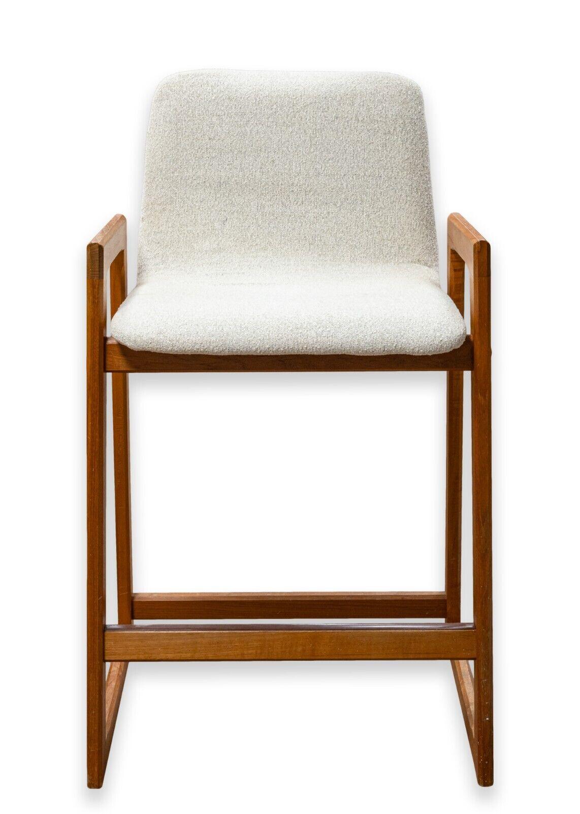 A pair of vintage mid century modern Danish barstools. A beautiful pair of Danish barstools featuring a gorgeous teak wood frame, and a white fabric upholstery. These chairs boast a wonderful silhouette with unique angular shapes and rounded edges.
