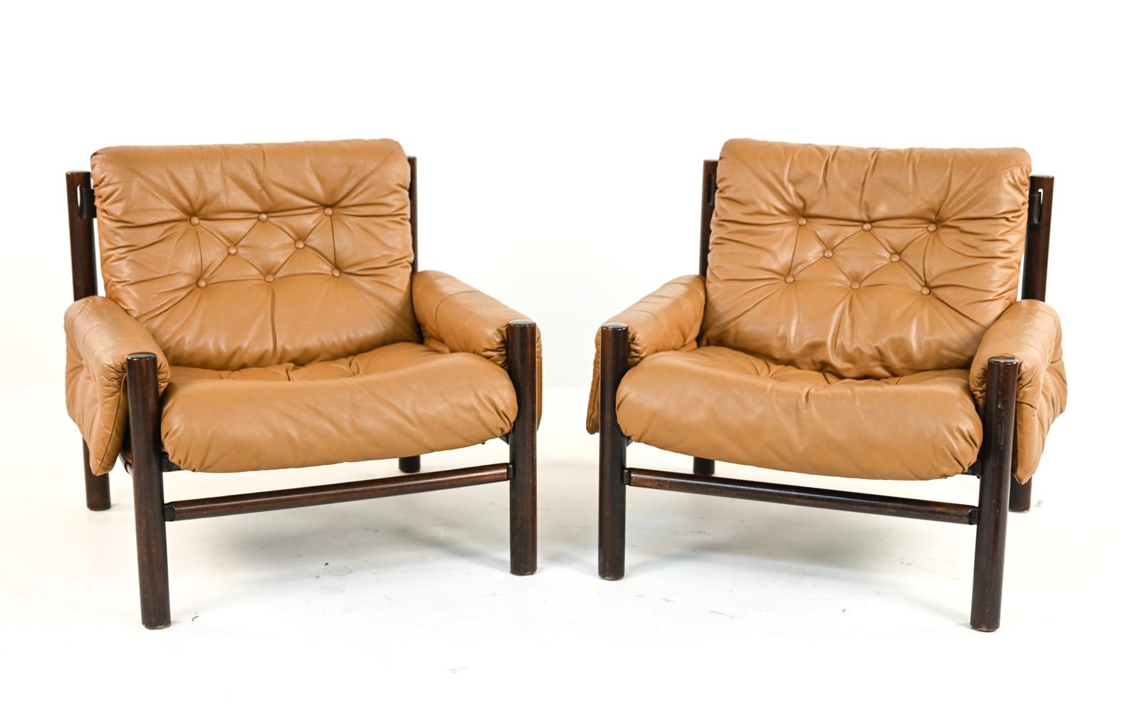 A handsome Danish mid-century pair of lounge chairs in the style of designers Percival Lafer and Arne Norell featuring rich butterscotch tufted leather cushions and a dark stained frame with interesting spindle backrests. These chairs feature many