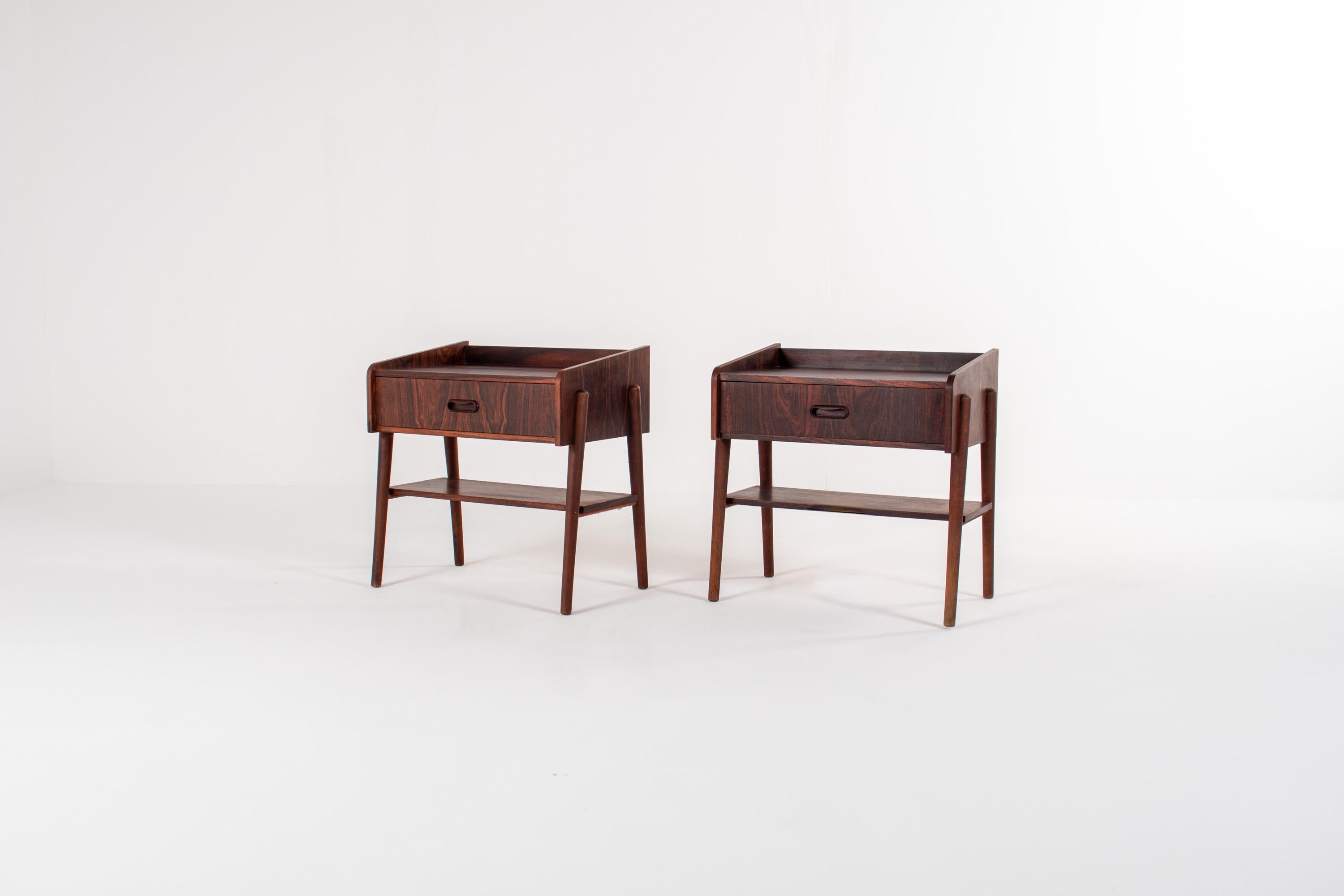 Beautiful pair of Danish mid-century bedside tables crafted in richly grained rosewood. These refined pieces feature a clean, elegant design typical of 1960s Scandinavian craftsmanship: rounded edges, integrated recessed handles, and a minimalist