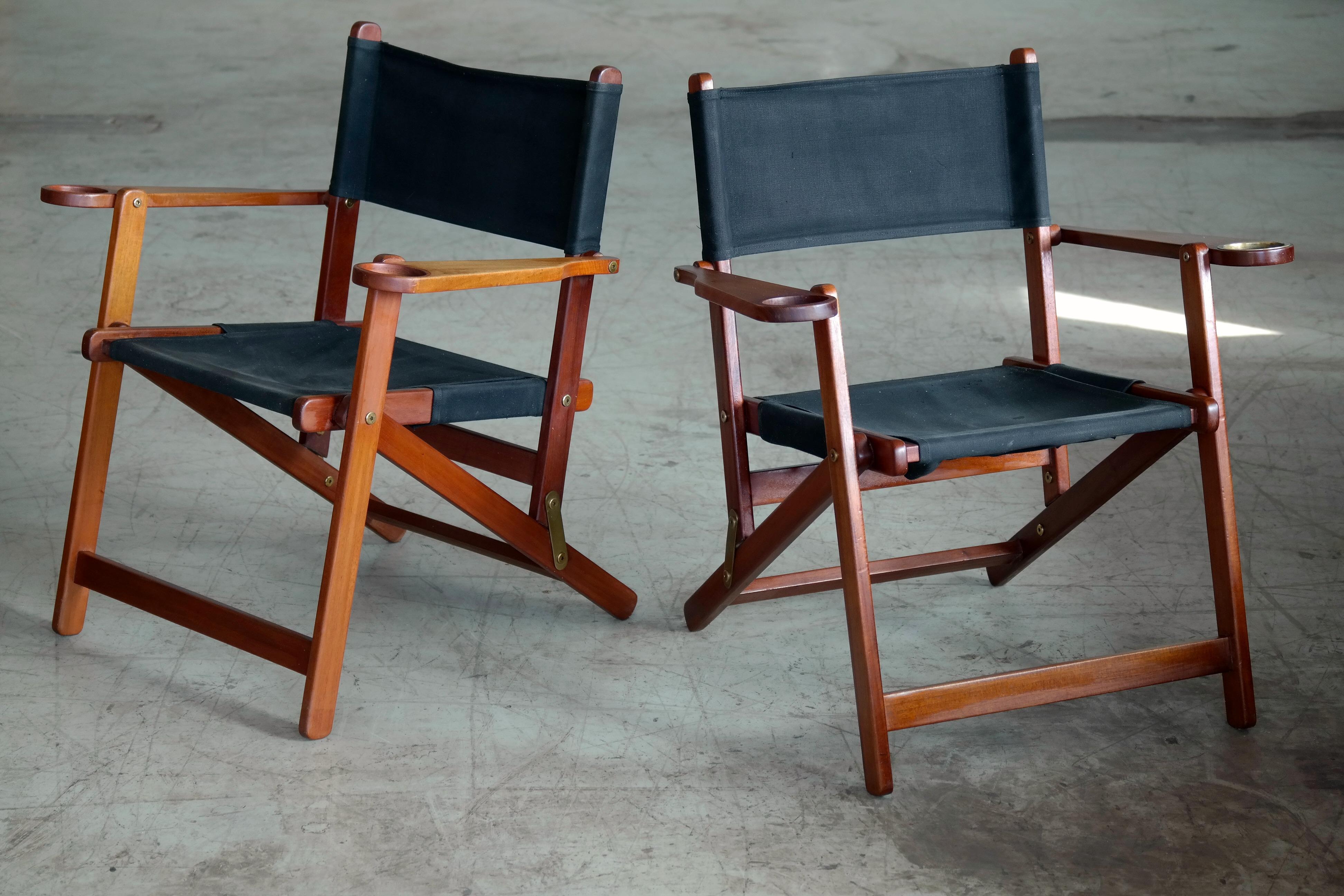 Unique and very charming folding deck chairs made in Denmark in the 1950s. Built in cup holders in armrests and one chair has a brass coaster. Very comfortable and sturdy made from solid teak on brass hinges with seat and backrest in black canvas.