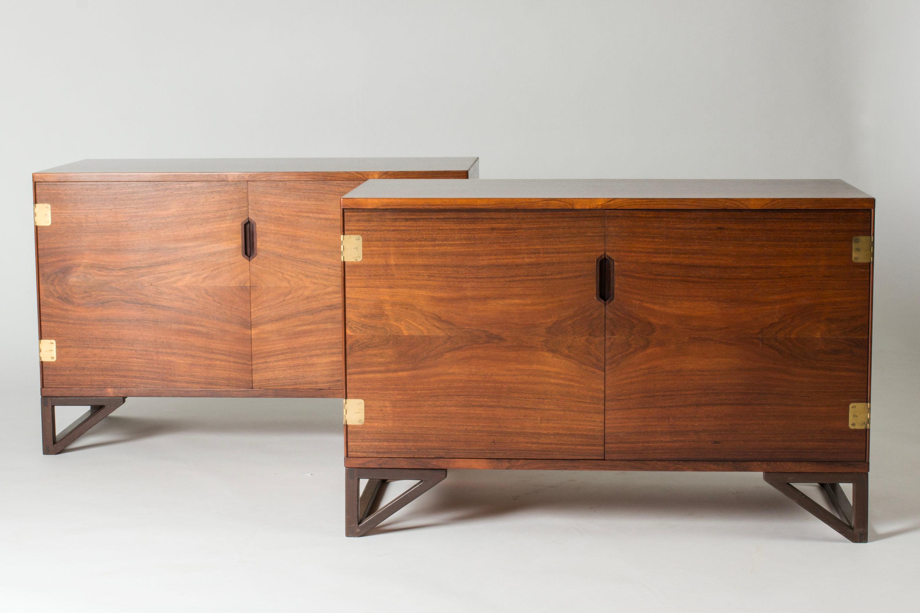 Pair of striking rosewood sideboards by Svend Langkilde in a neat size. Cool, graphic legs forming triangle shapes, decorative sculpted opening. Distinct brass hinges. One of the sideboards has drawers to one side inside. The same sideboard has had