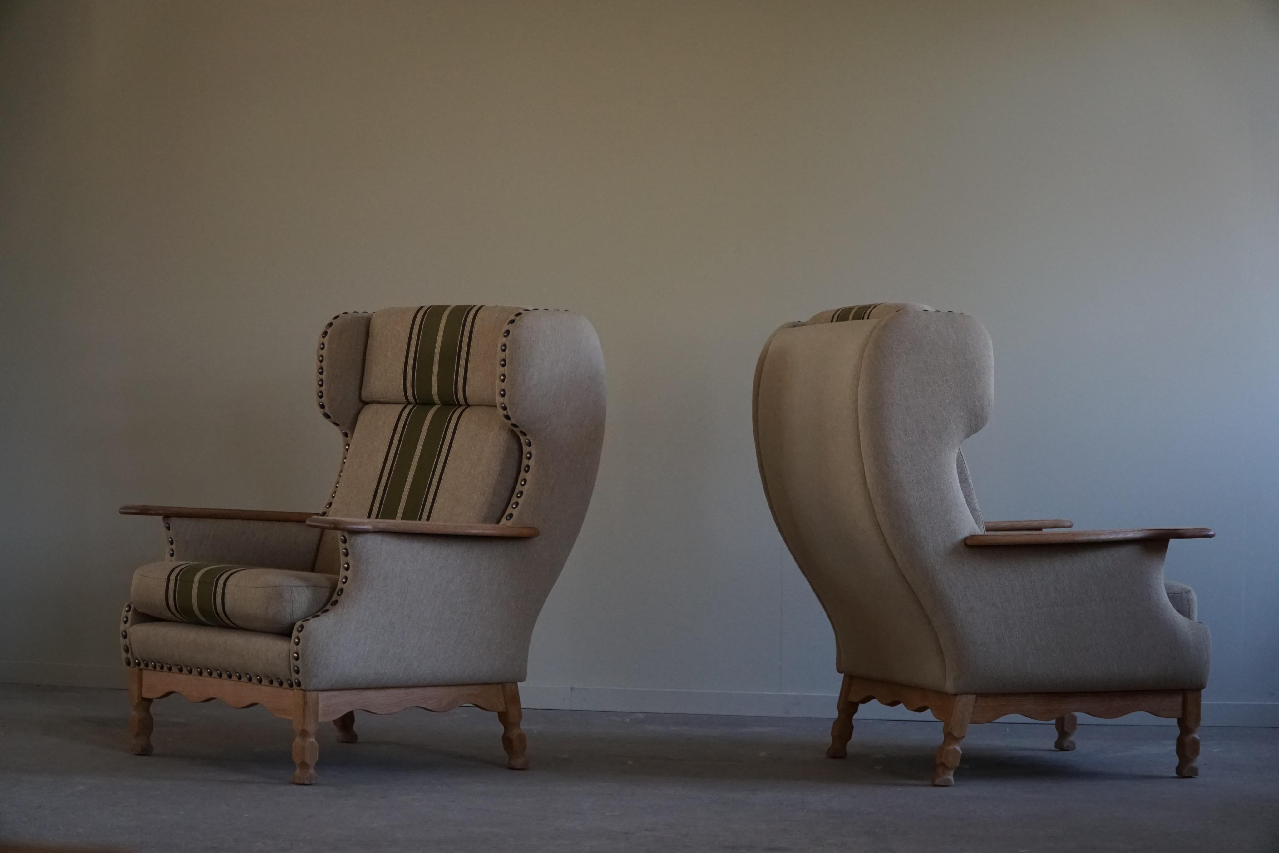 Ein skulpturales Paar komfortabler Lounge-Sessel mit hoher Rückenlehne, die aus hochwertigen Materialien gefertigt sind und in ihrem Stil an die Arbeiten des dänischen Designers Henning Kjærnulf erinnern. Die Armlehne ist aus dem gleichen Eichenholz