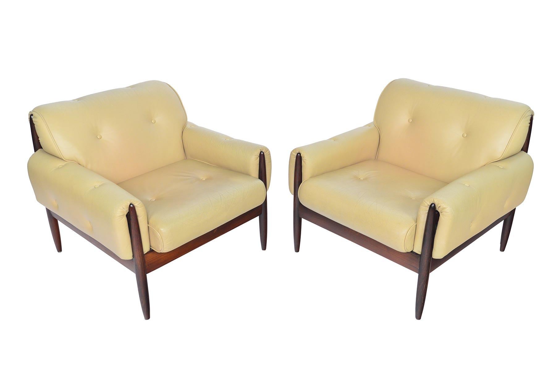 This beautiful pair of Brazilian rosewood lounge chairs offer an elegant silhouette with exceptional wood trim. Upholstered on all sides, this pair features large sculpted rosewood frame. The pair wear their original cream leather cushions. The